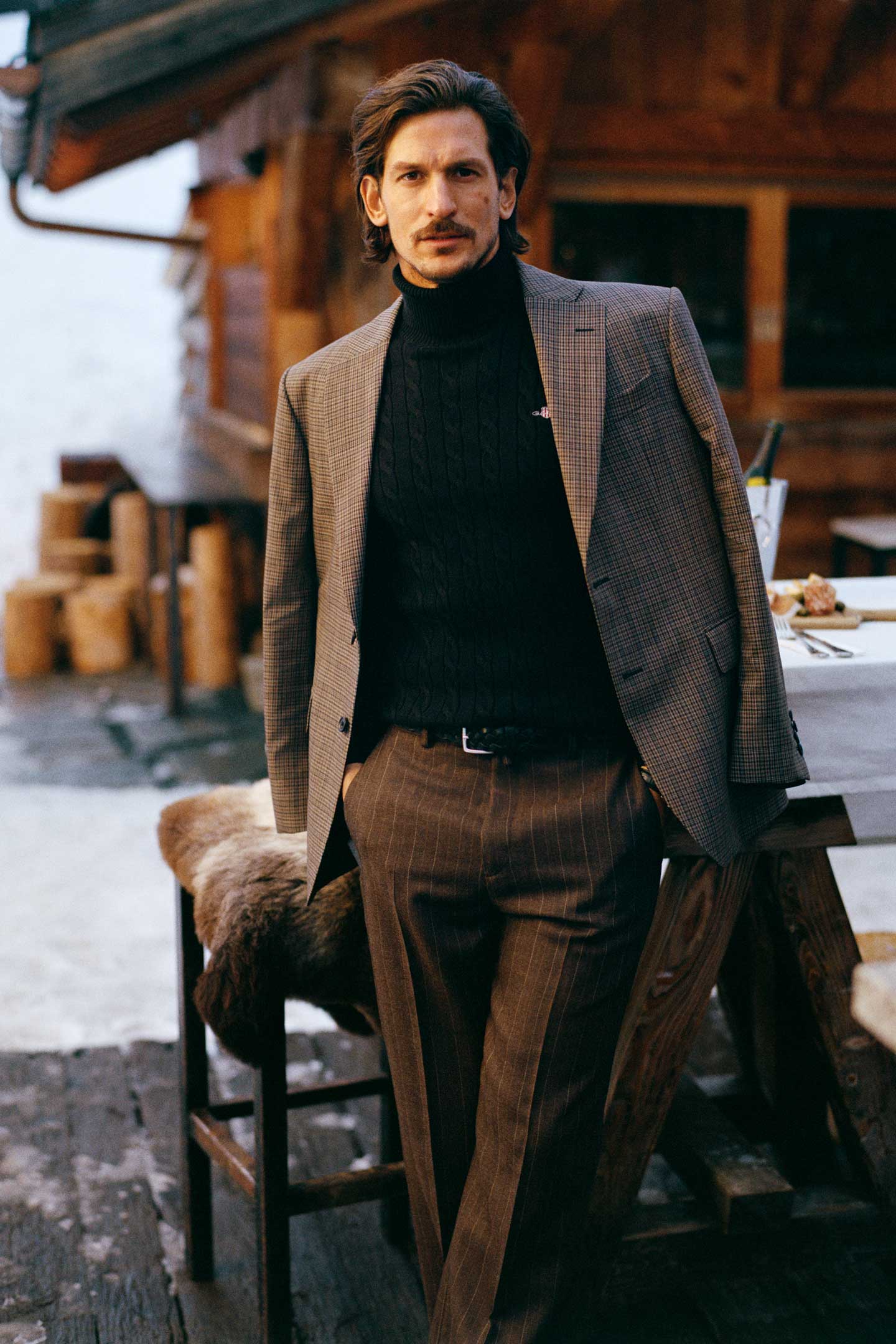 Model styled in a Gant checked blazer layered over a cable-knit roll-neck sweater and pinstripe pants.