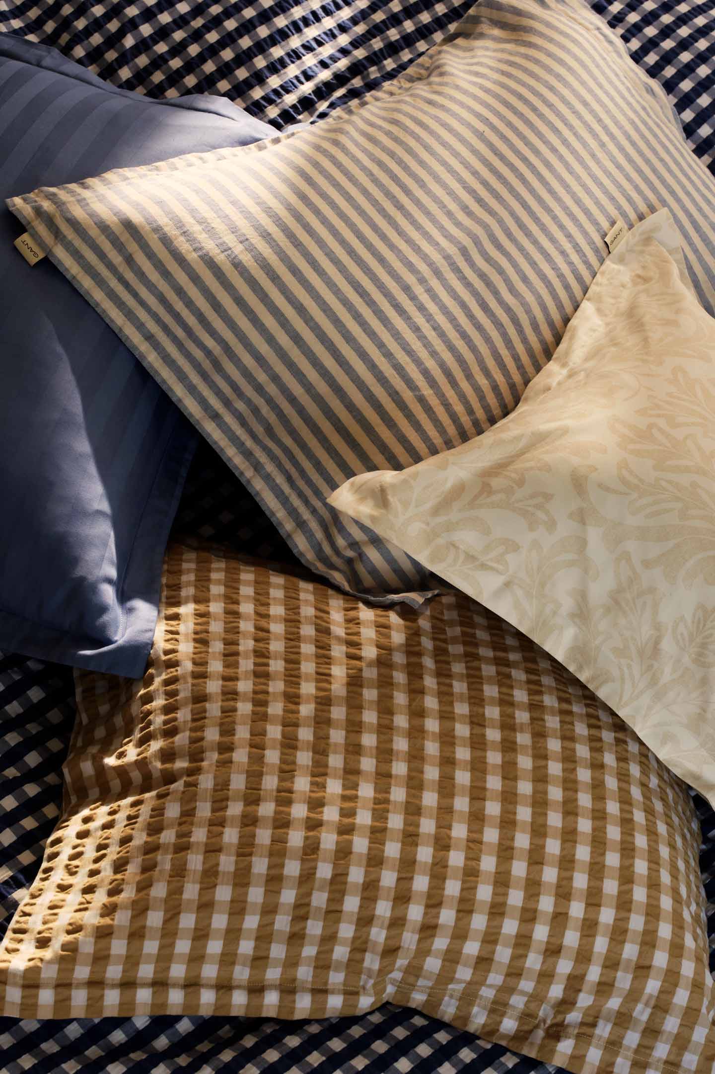 Gant striped and checked pattern pillows arranged on a bed.