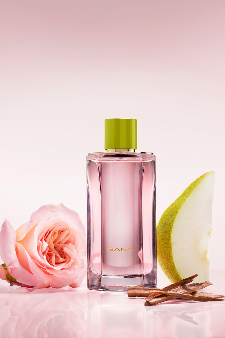 Flacon de parfum GANT rose, présenté avec une rose, un quartier de poire et des bâtonnets parfumés