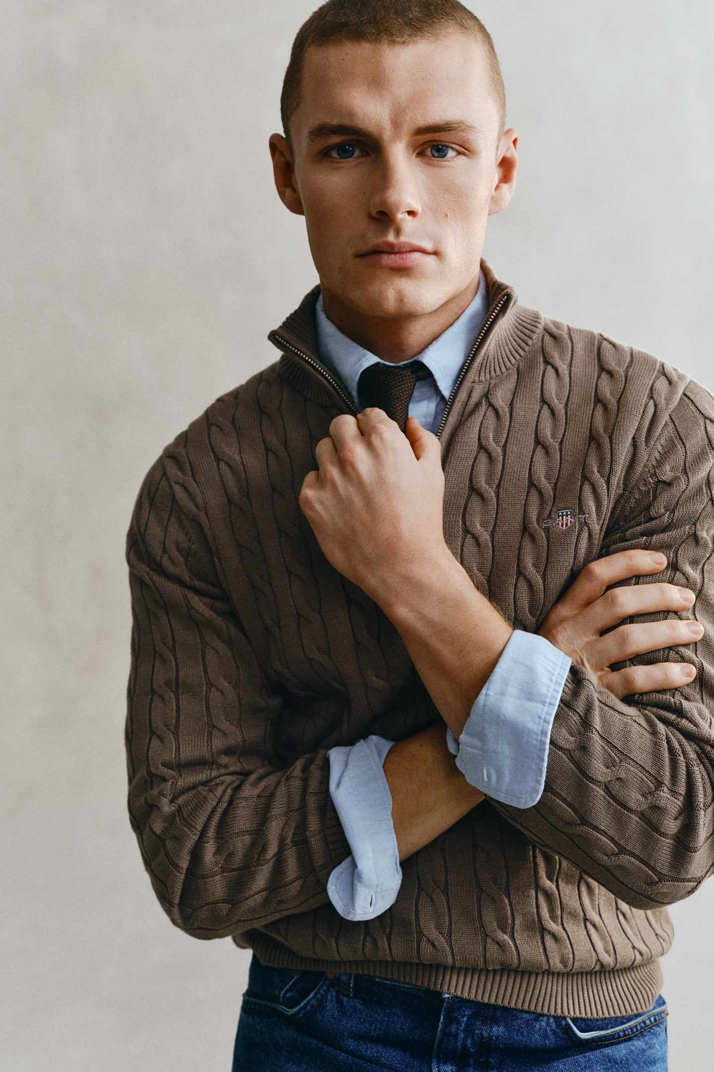 Model styled in a GANT brown cable knit layered over a blue shirt and striped tie.