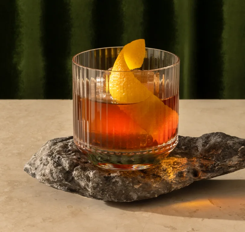 A cocktail in a rocks glass with a large twisted orange peel garnish
