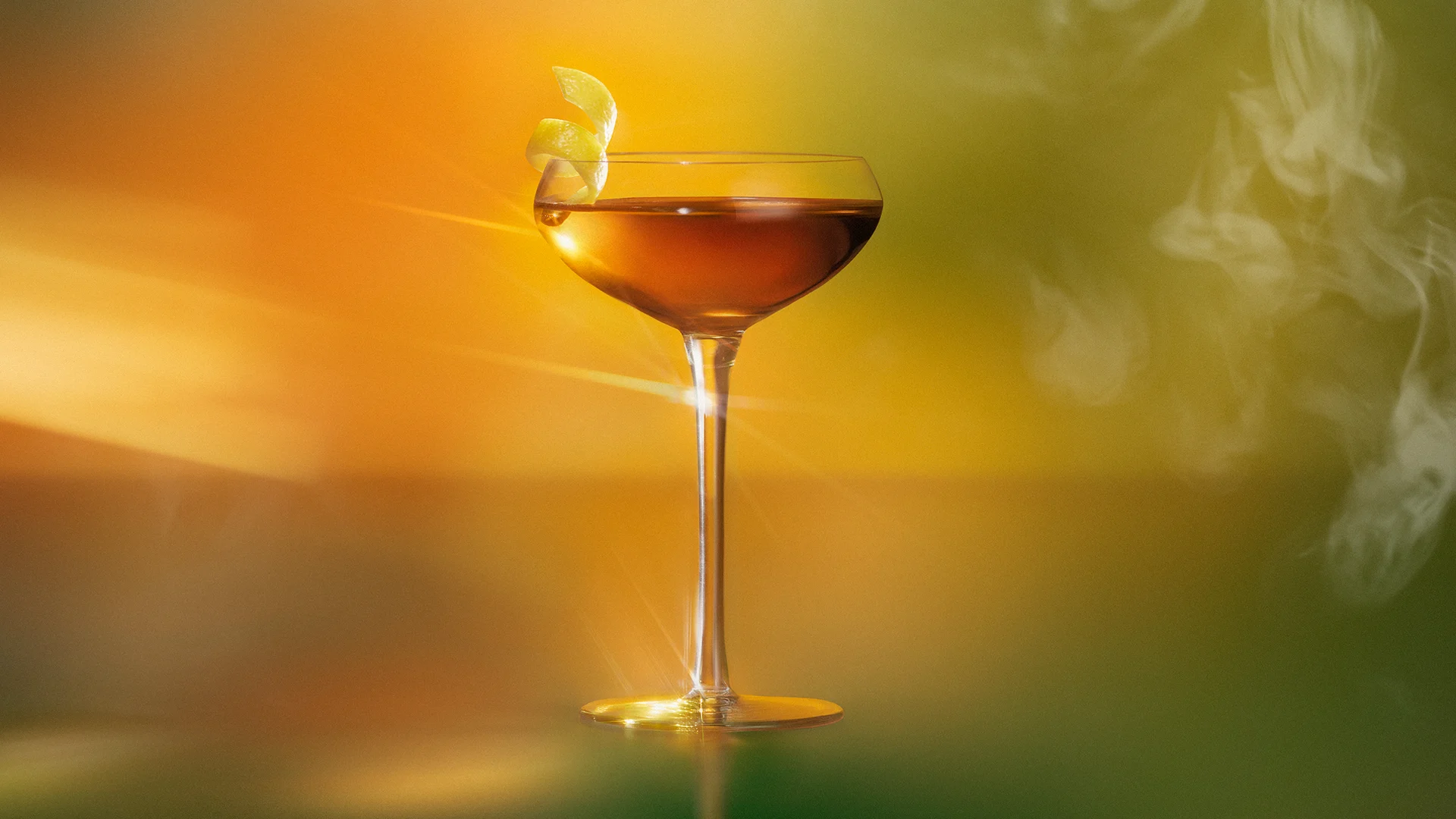 Lagavulin Sweet Peat Tea cocktail served in a coupe glass with lemon twist, showcasing the whisky's golden amber color against a warm gradient background.