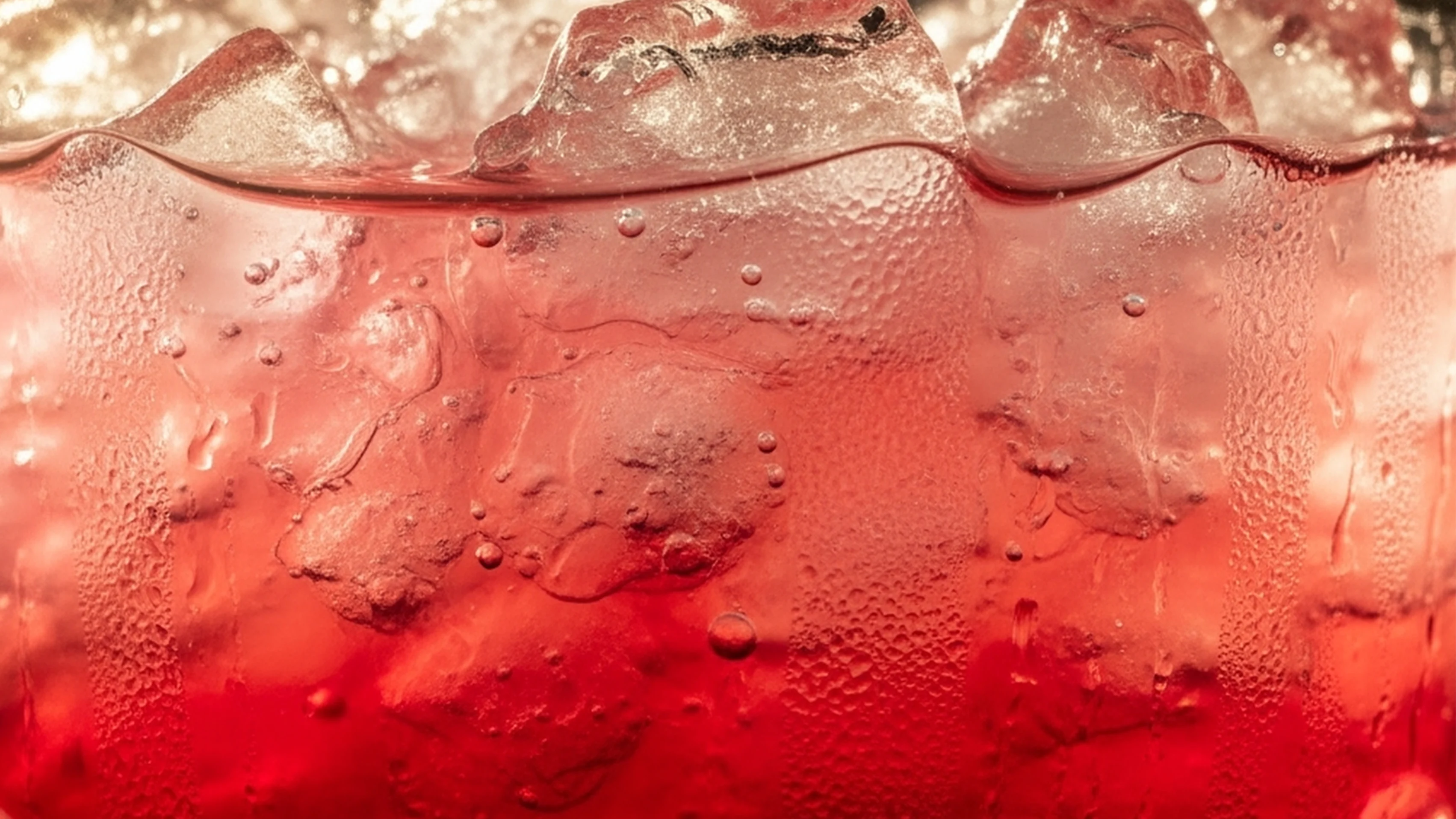 A close up of a red-purple liquid in a glass with ice and bubbles
