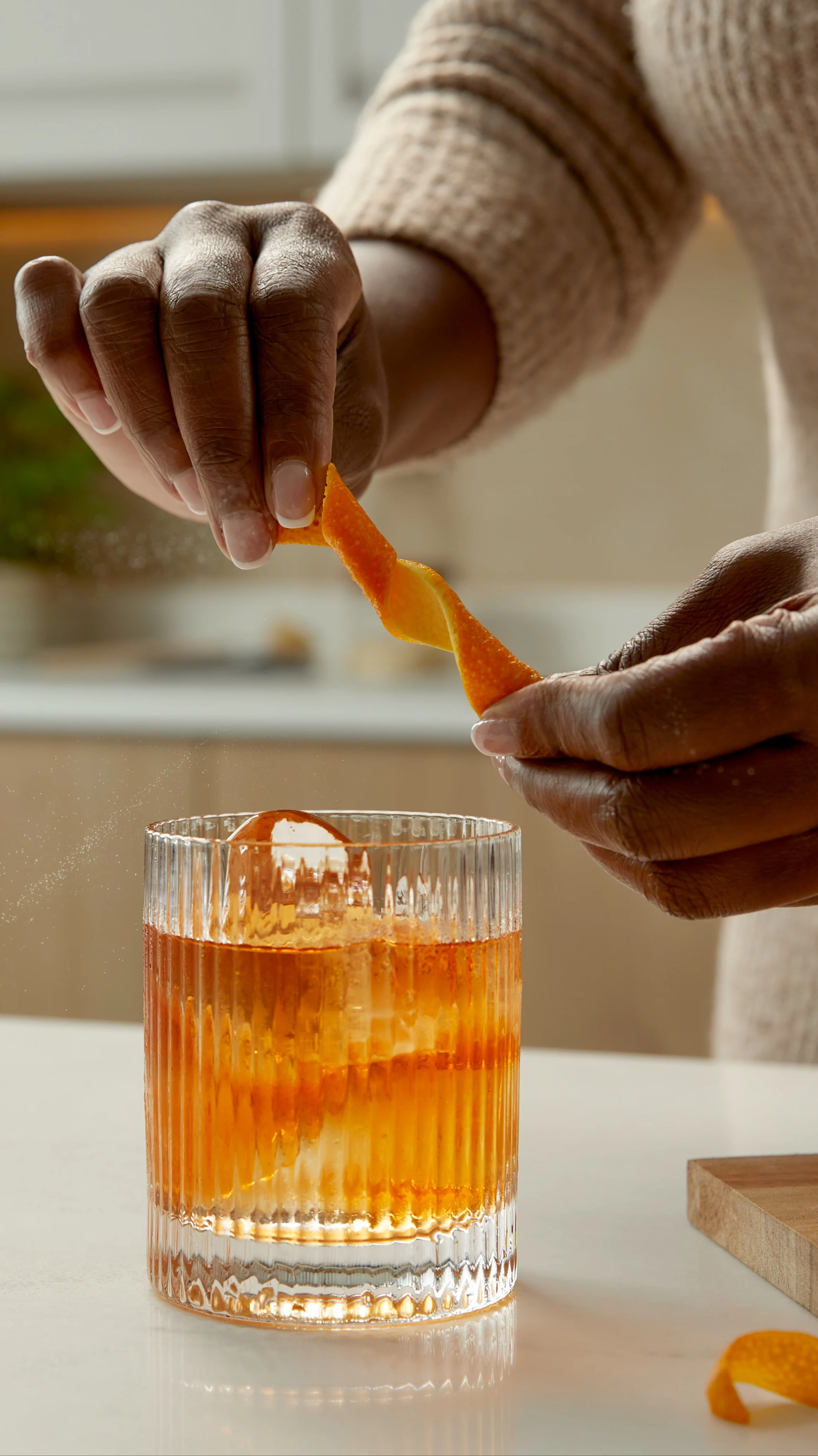 Iemand draait een sinaasappelgarnering boven een Old Fashioned cocktail in een ijsglas.