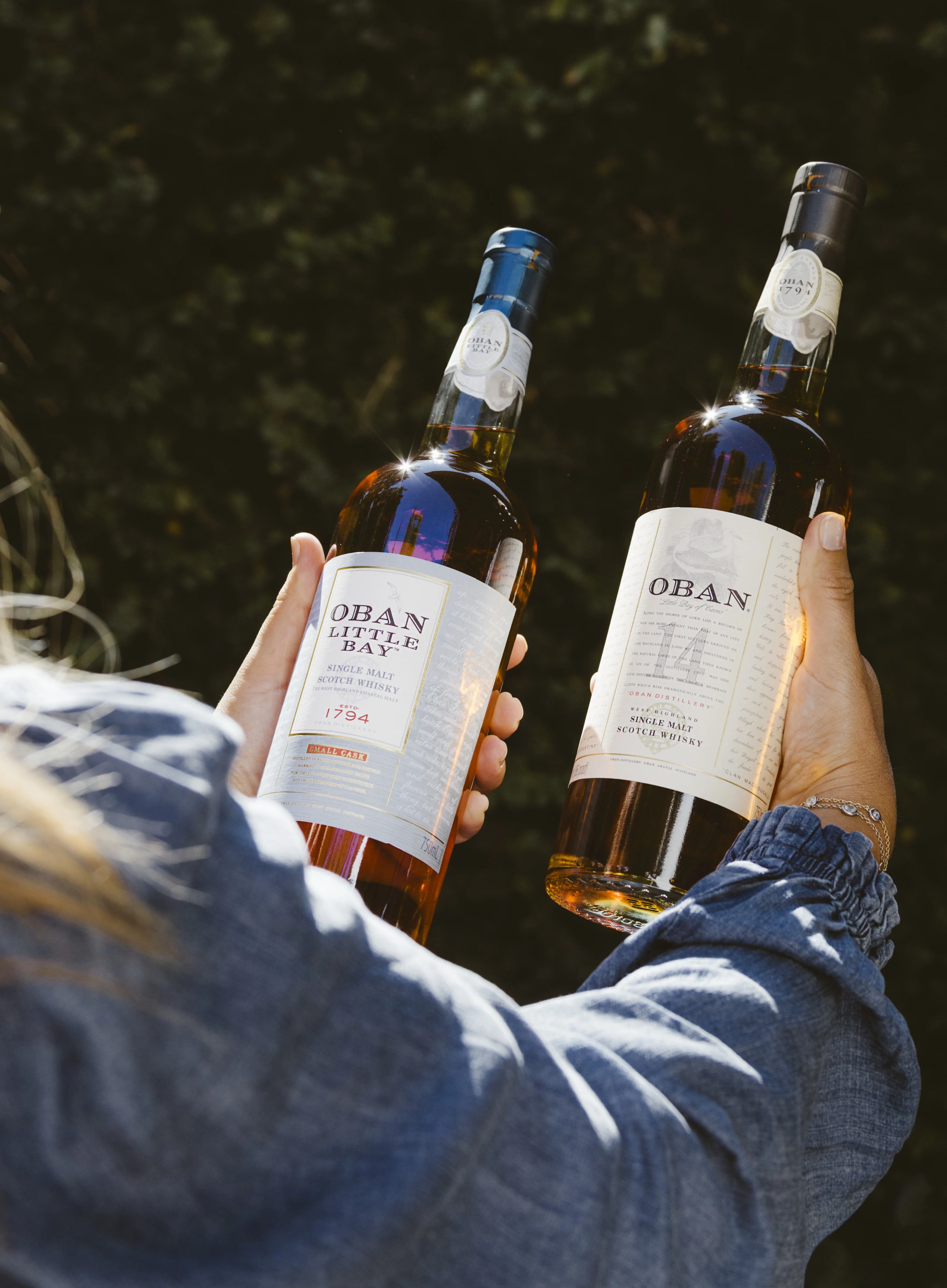 A woman holds two bottles of Oban whisky outside.