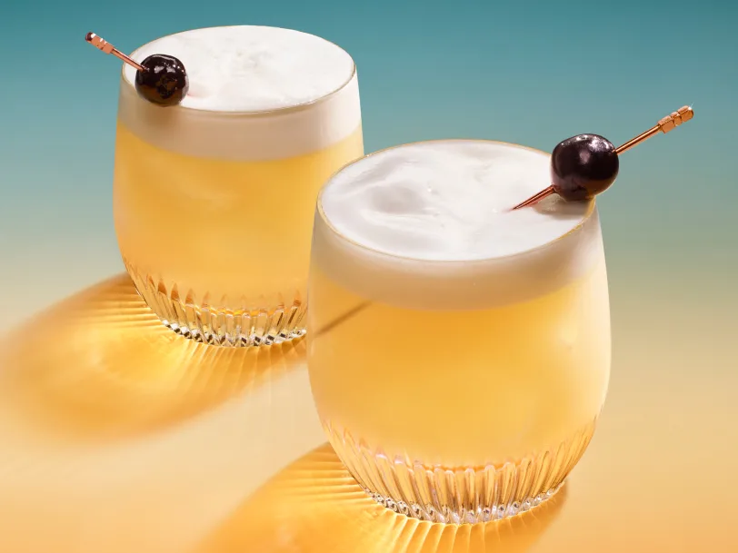 Two sour cocktails in rocks glasses with skewered maraschino cherry garnishes