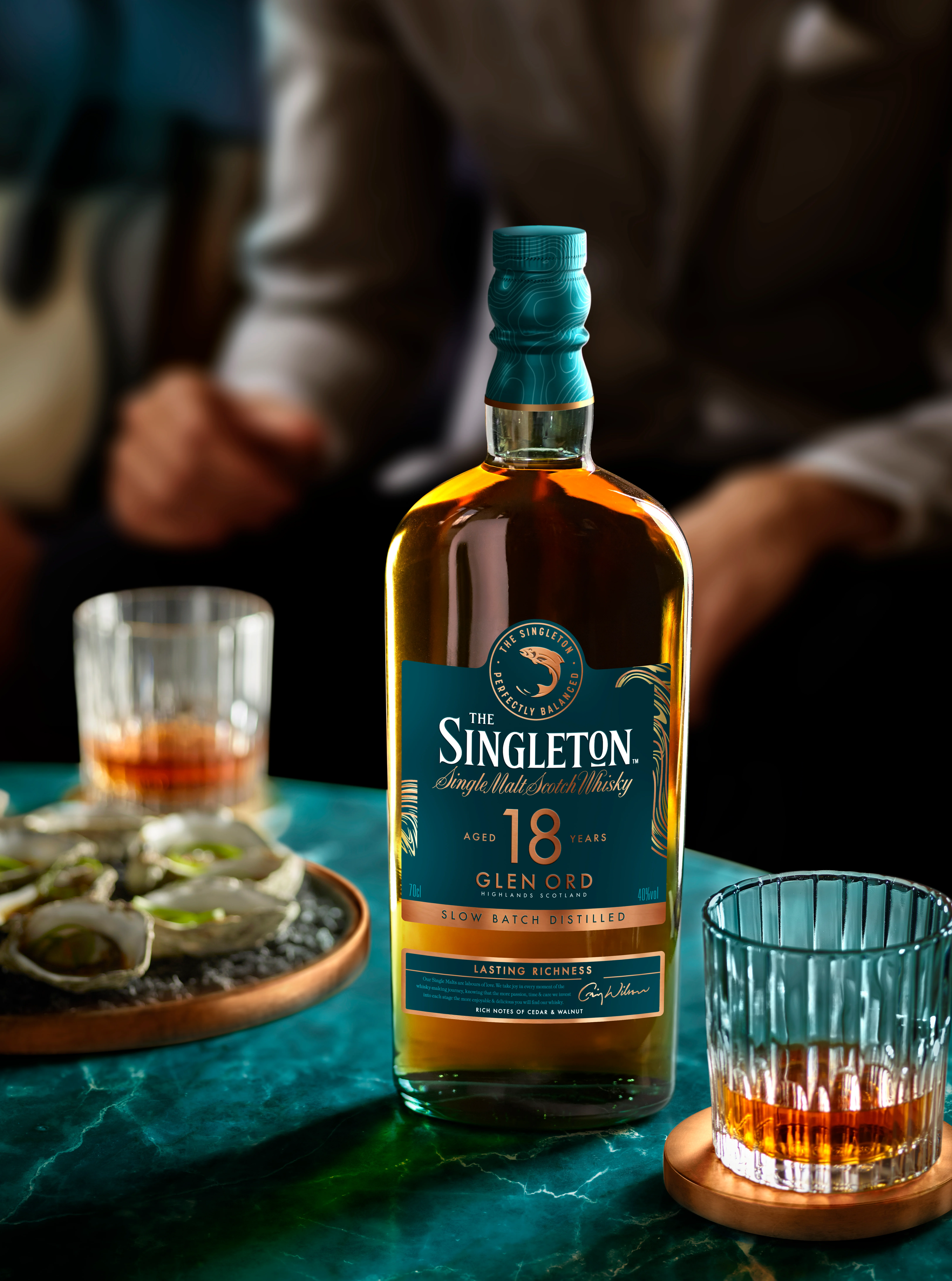 The Singleton of Glen Ord 18 Year Old Single Malt Scotch Whisky Bottle and a serve in a tumbler glass on a teal table