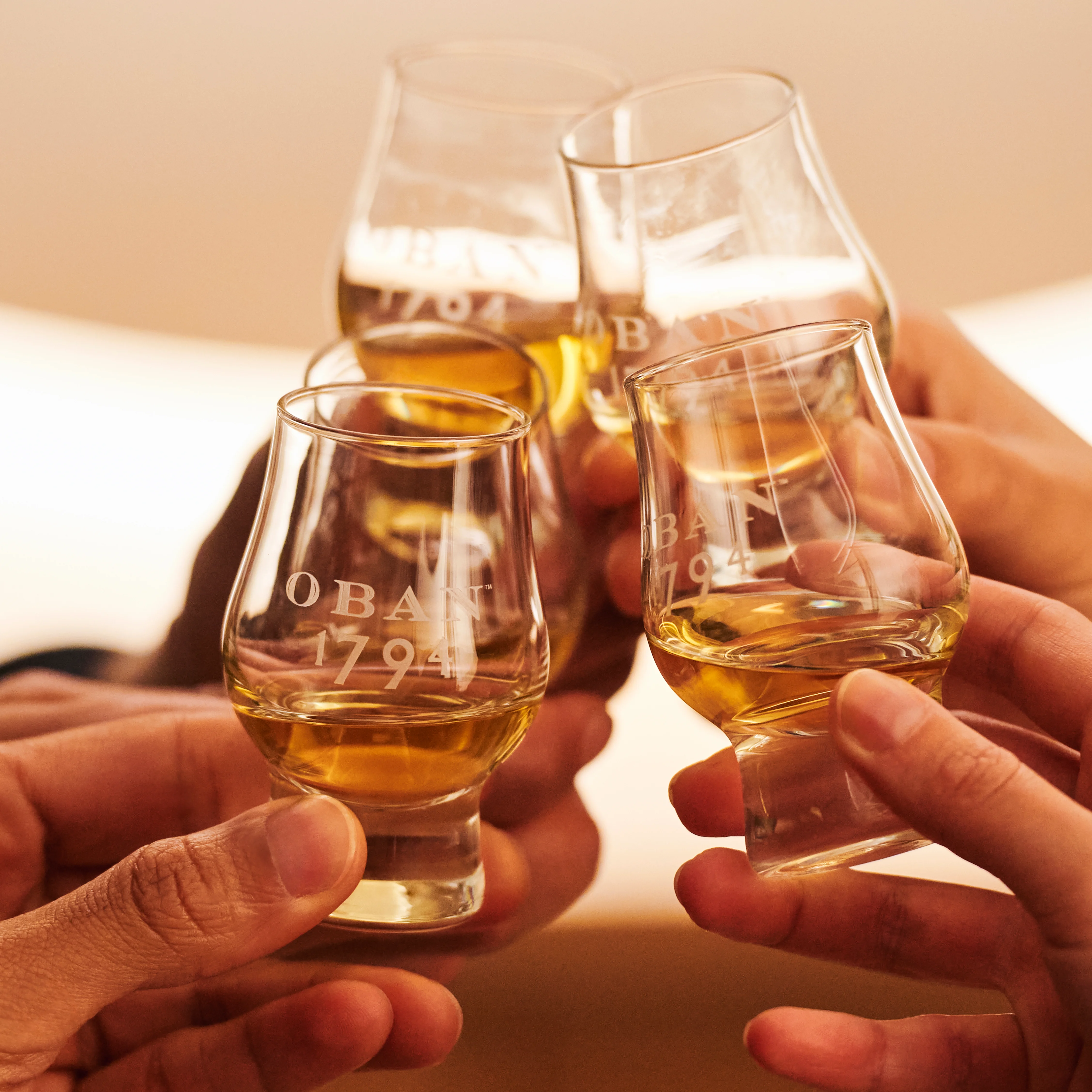 Four glasses of Oban whisky being held in a cheers
