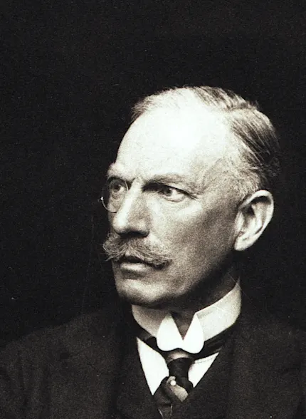 Ein Mann mit Monokel in edwardianischer Kleidung mit Jacke, Weste, Krawatte und steifem weißen Kragen.