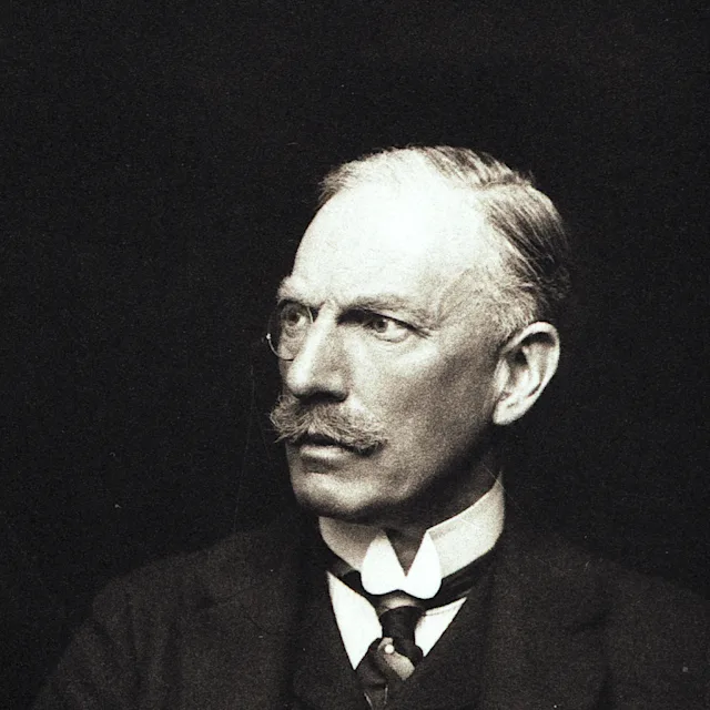 A man with a monocle in Edwardian dress with a jacket, waistcoat, tie and stiff white collar.