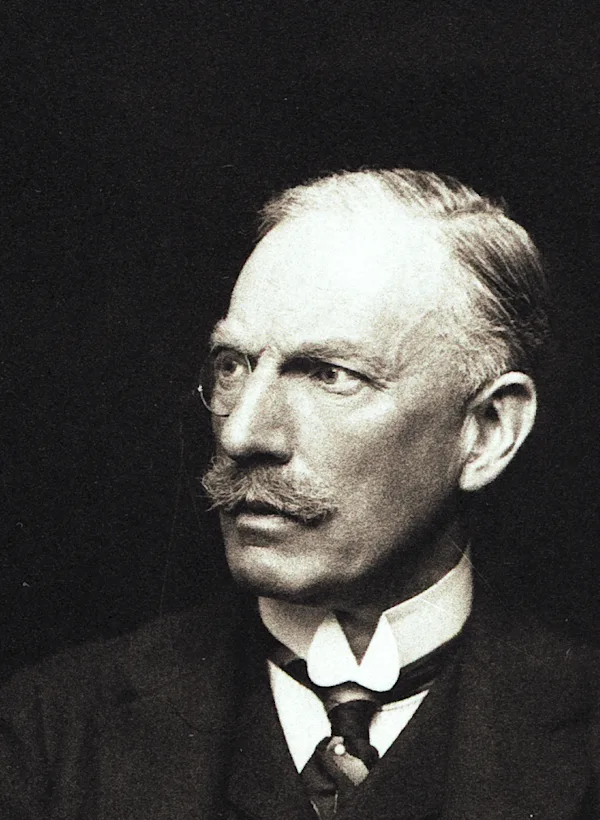 一位戴著單片眼鏡的男子,穿著愛德華時代的服裝,外套、馬甲、領帶和硬挺的白領。