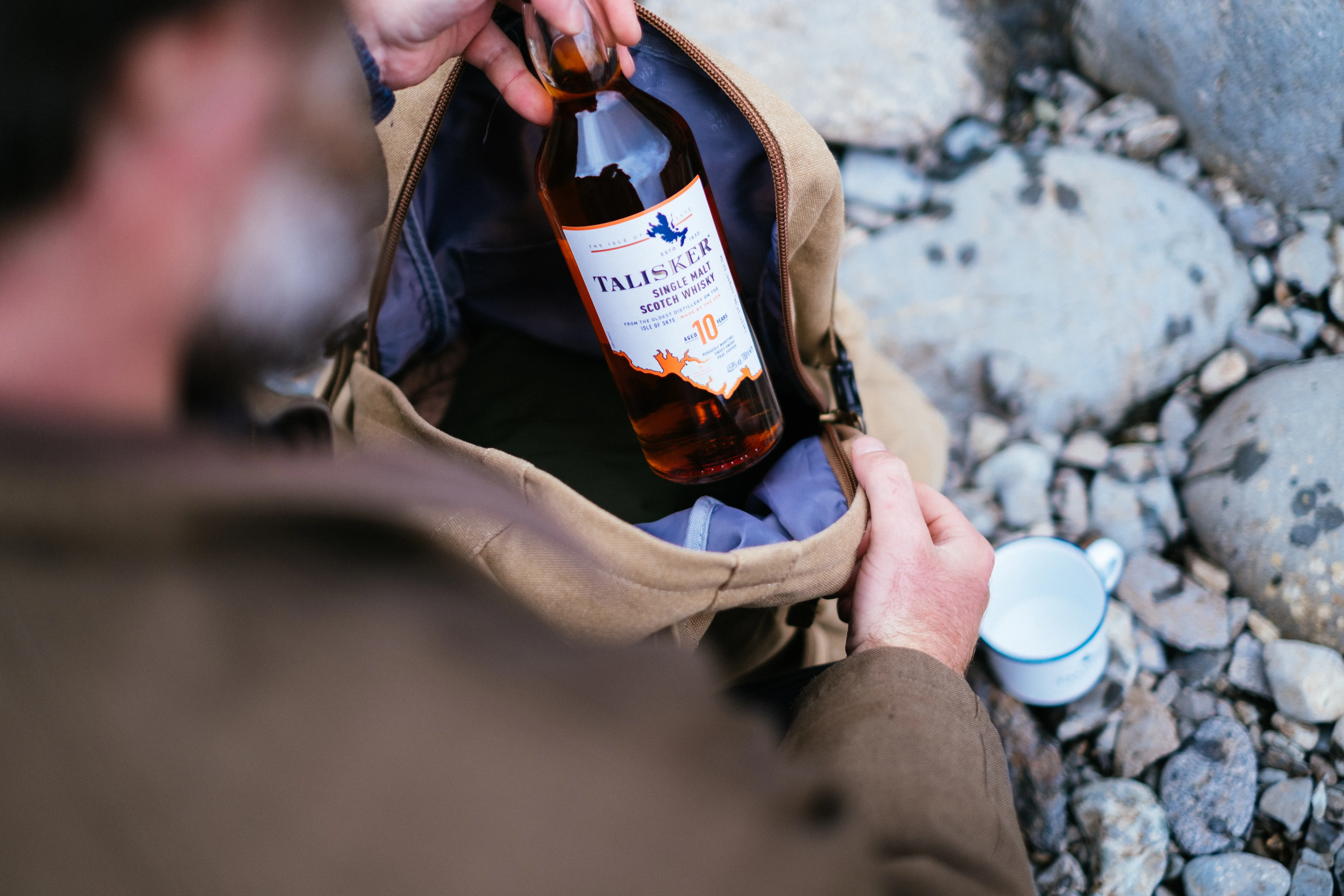 A person takes a bottle of Talisker 10 year old whisky out of a rucksack at the seaside