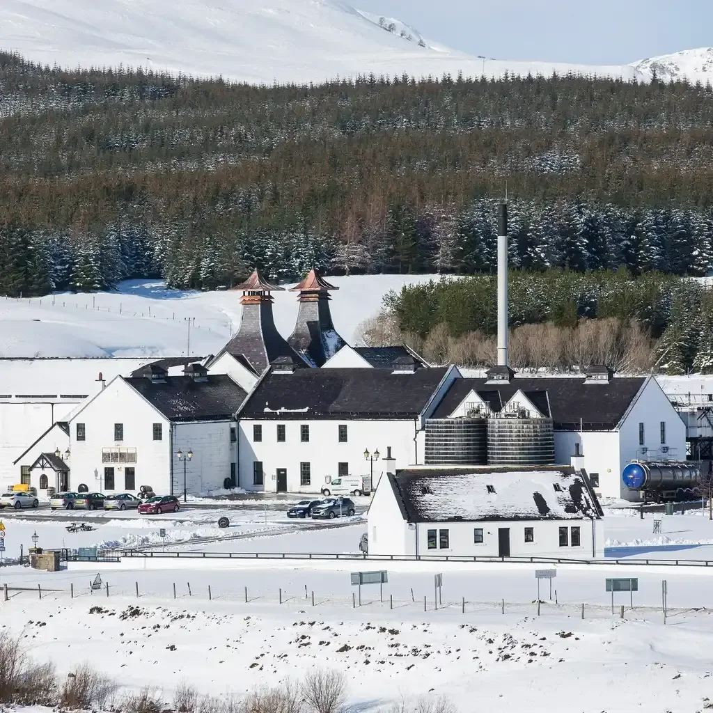 Outside view of Dalwhinnie Distillery with the mountains in the background covered with snow