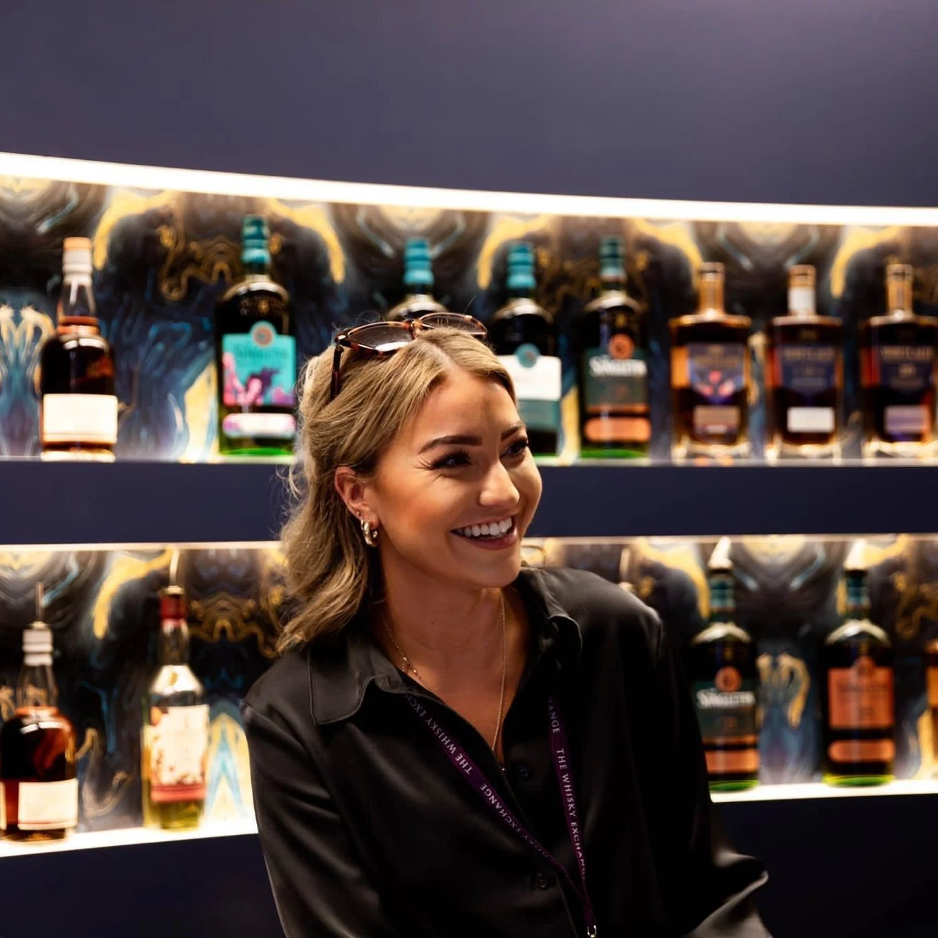 Een portret van whiskyexpert Kirsty Thomson voor een verlichte bar met whiskyflessen.
