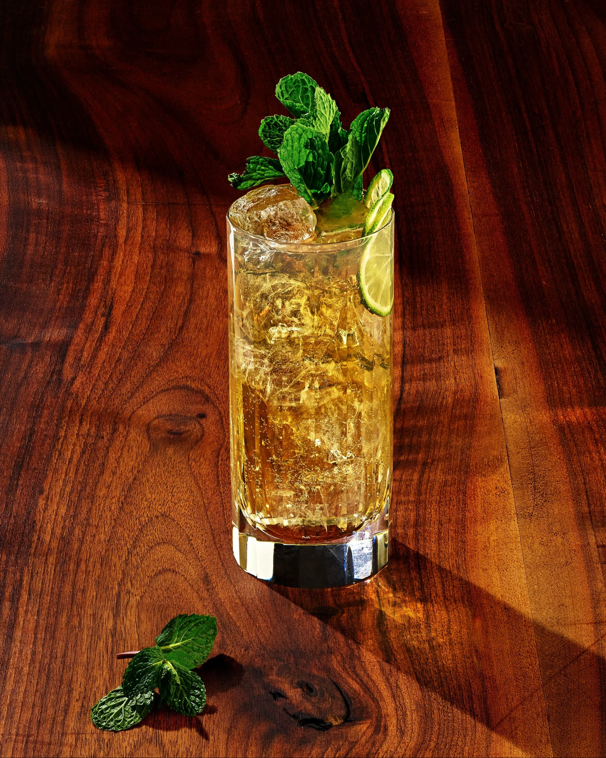 Light brown liquid in a highball glass with ice and a garnish of mint leaves