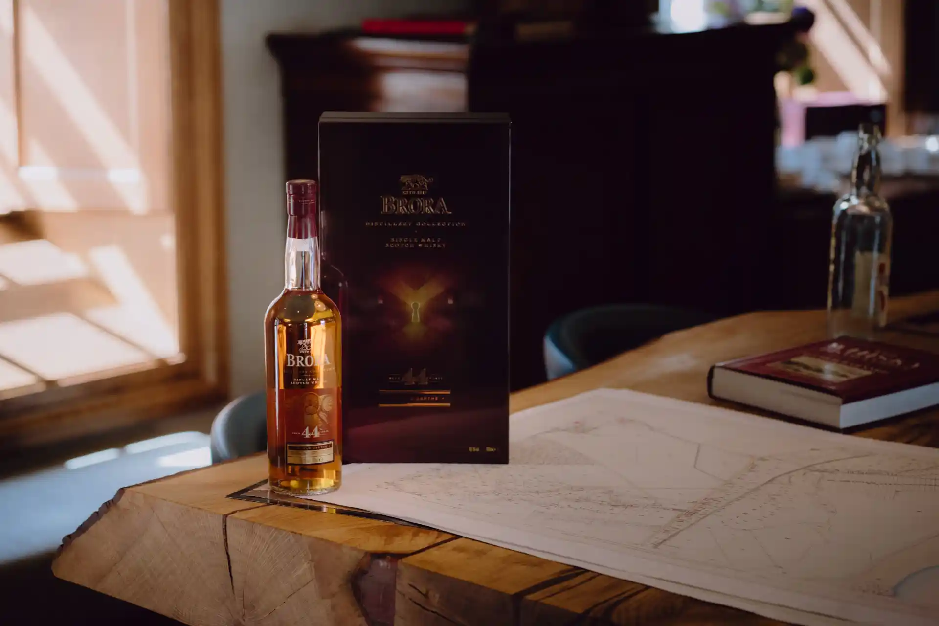 A bottle and case of a 44 year old Brora Single Malt Whisky sits on a map on a wooden table in a sunlit room.