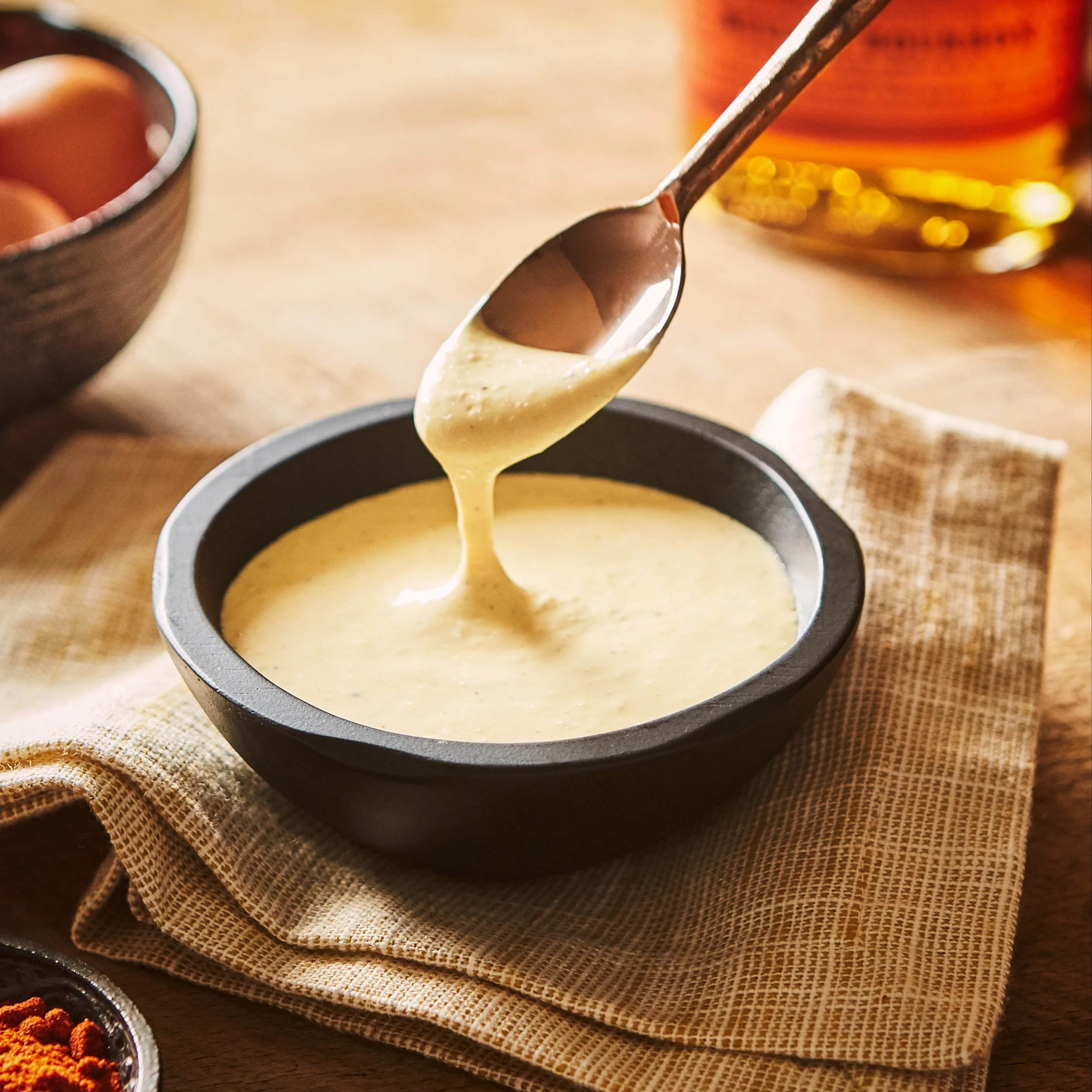 A silver spoons stirs a bowl of white whisky sauce.