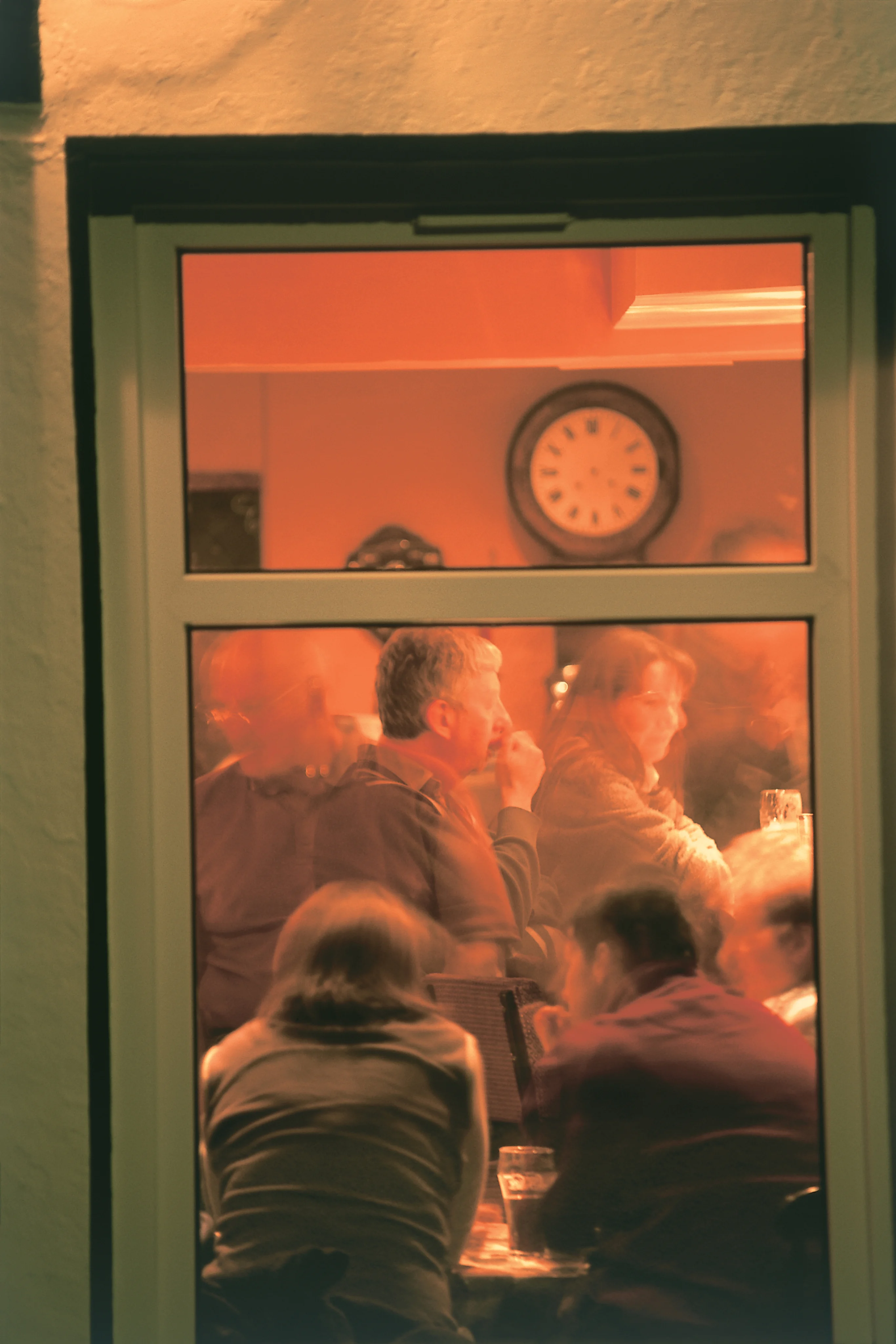 People sitting inside a warmly lit whisky bar or tasting room viewed through a window.