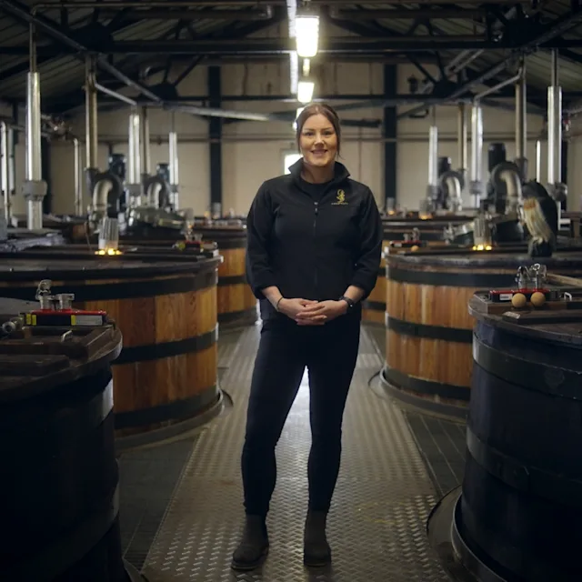 A distillery worker stands surrounded by whisky casks