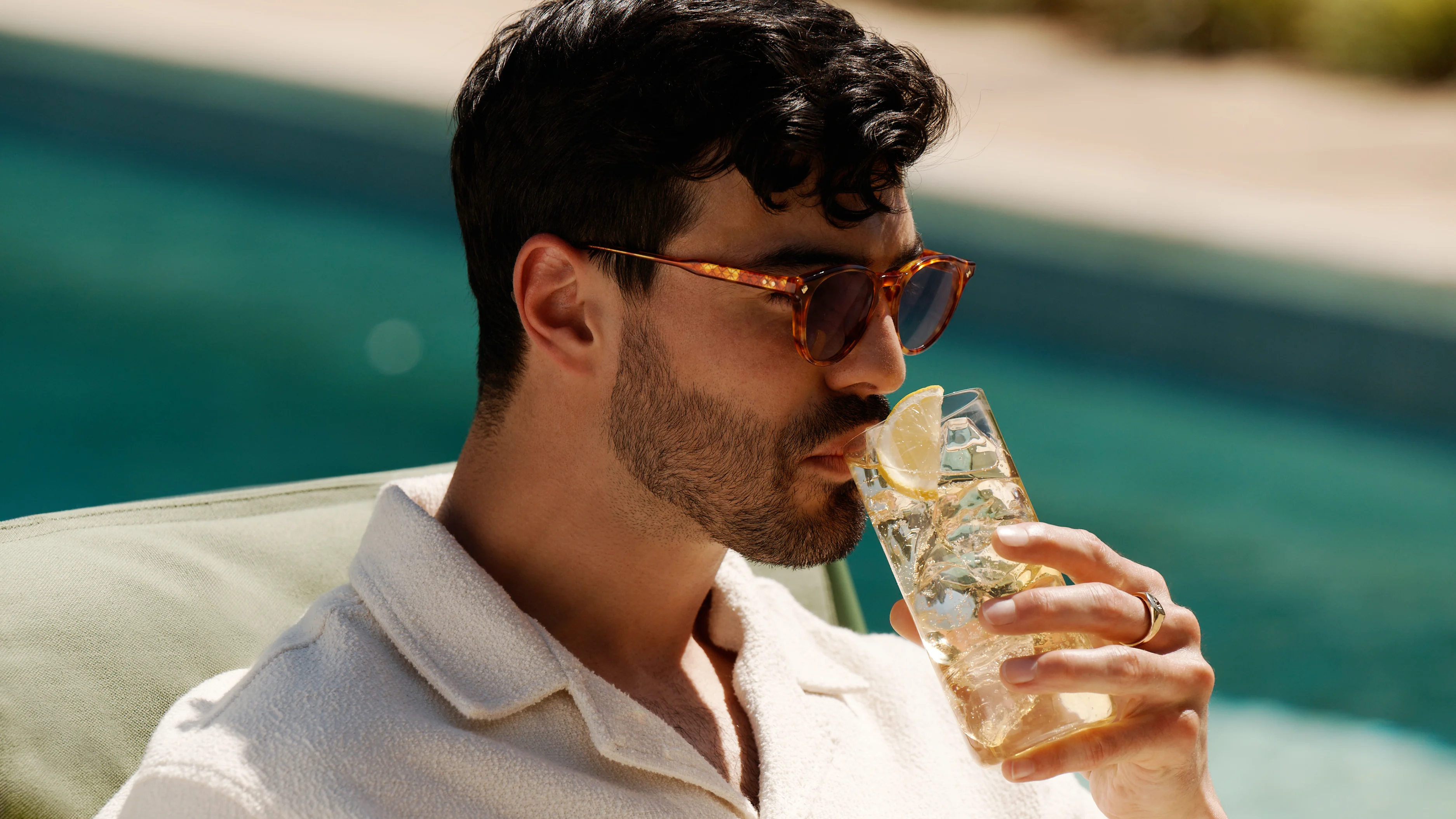 Ein Mann sitzt an einem Pool und nippt an einem Whisky-Highball-Cocktail