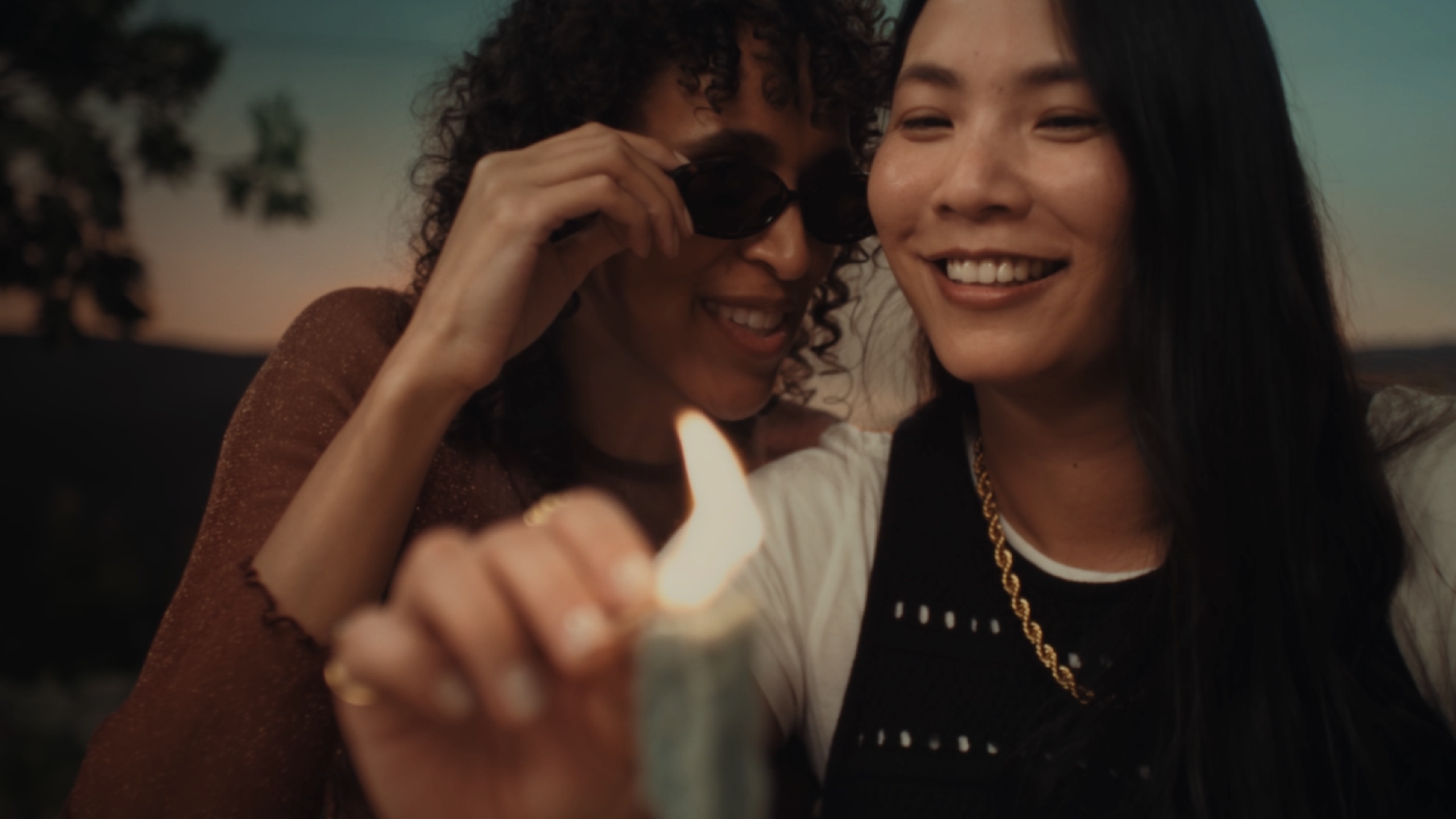 Two women enjoying a moment together, one holding a lighter, with a joyful atmosphere