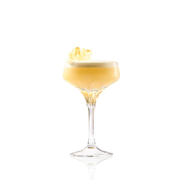 A light yellow cocktail in a coupe glass, with a white foamy top and a dried pineapple slice garnish