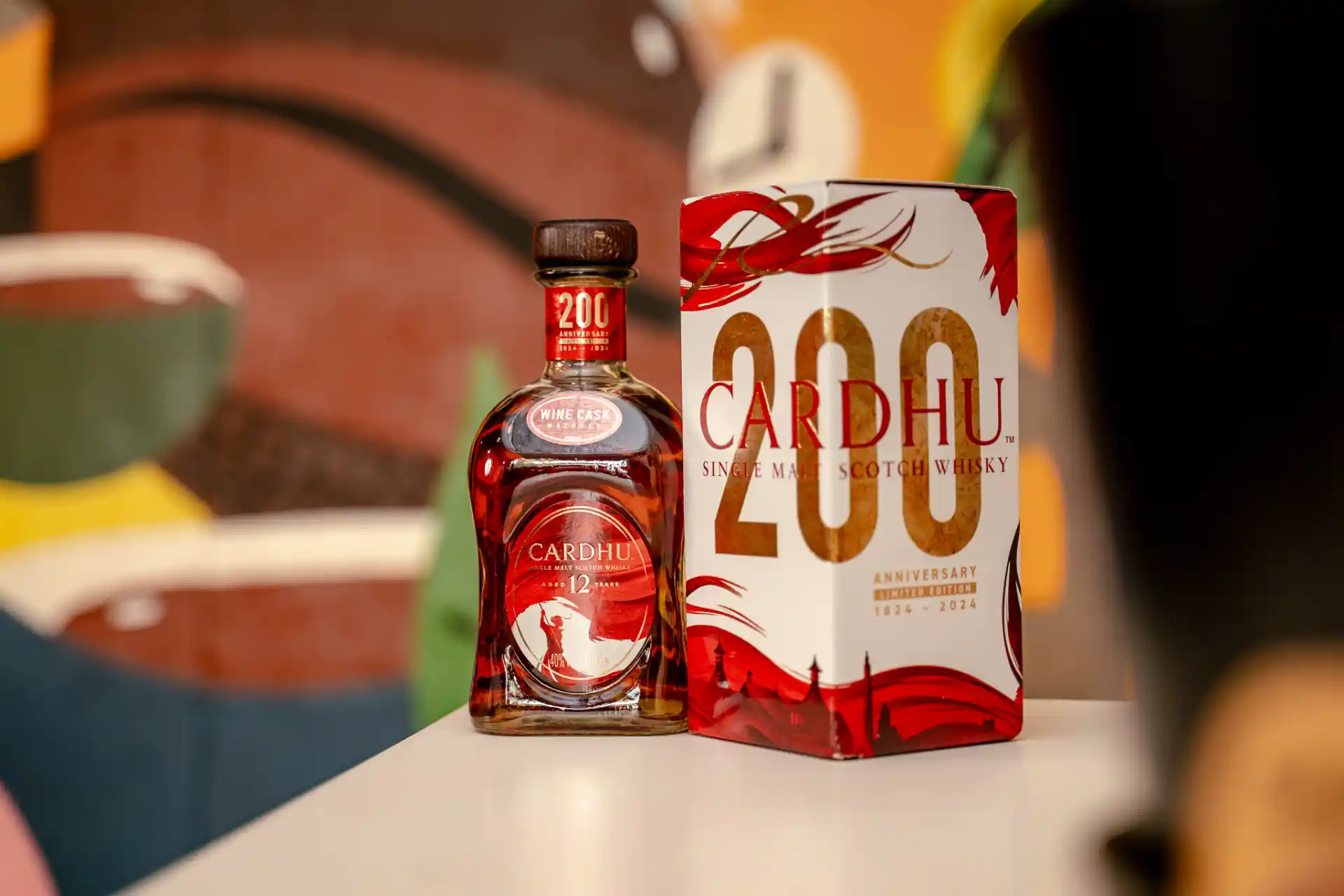 A bottle and the packaging of the 200th anniversary limited edition Cardhu Single Malt Scotch Whisky sit on a table.