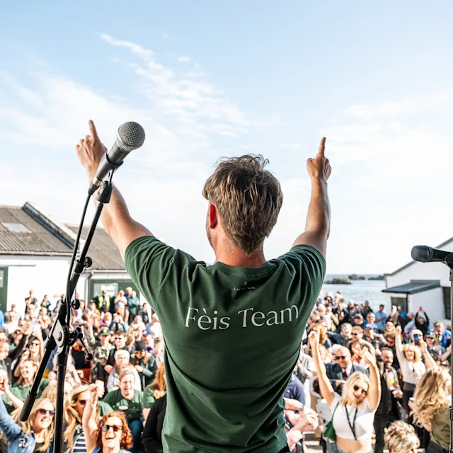 Discover the Fèis Ìle Festival Man standing on stage in a green shirt at Féis Ile festival hyping the audience up.