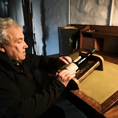 威士卡專家 Iain McArthur 坐在木桌前,桌上放著一瓶 Lagavulin 威士卡。