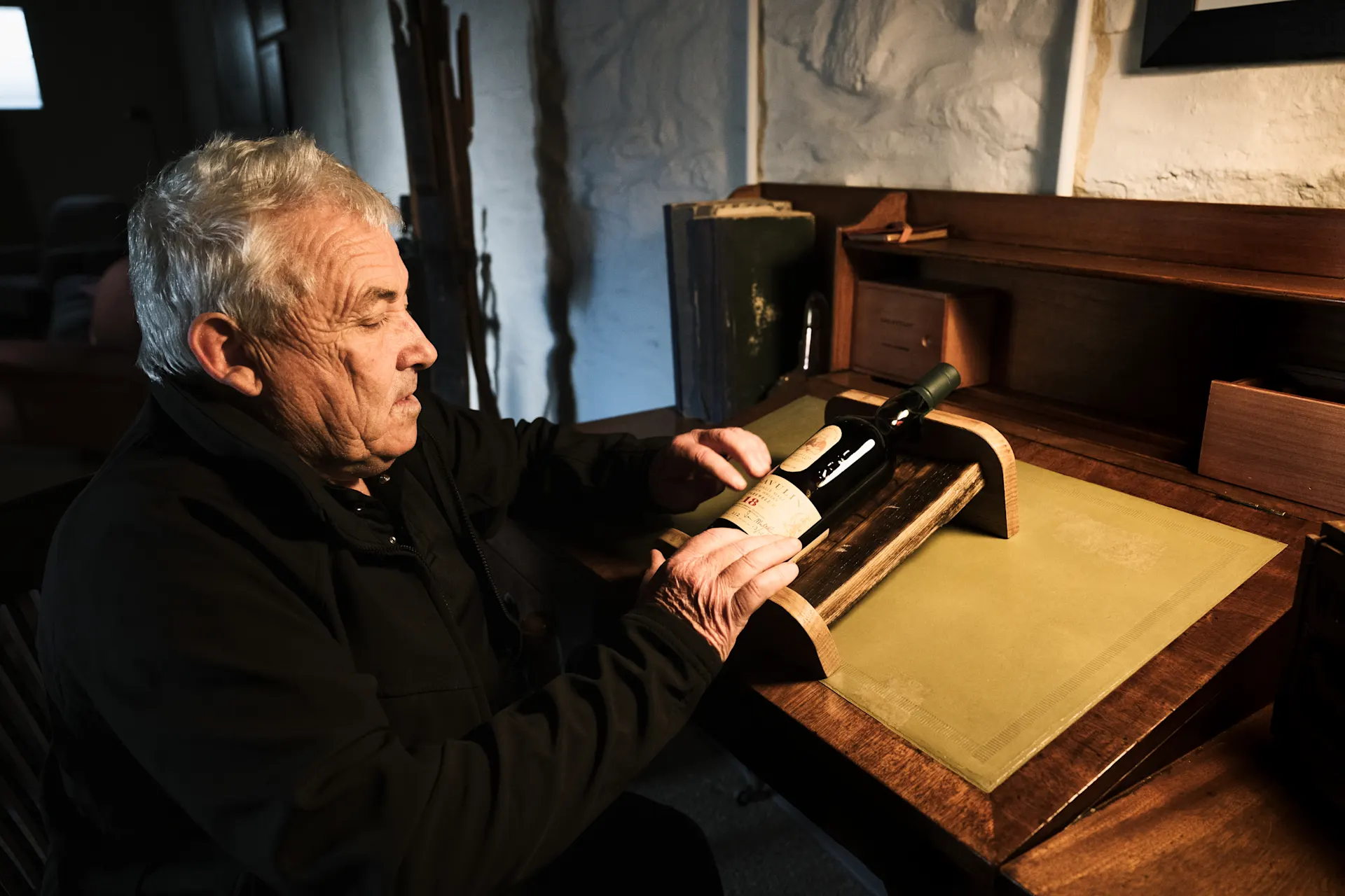 Whisky-expert Iain McArthur zit voor een houten bureau, waarop een fles Lagavulin whisky staat.