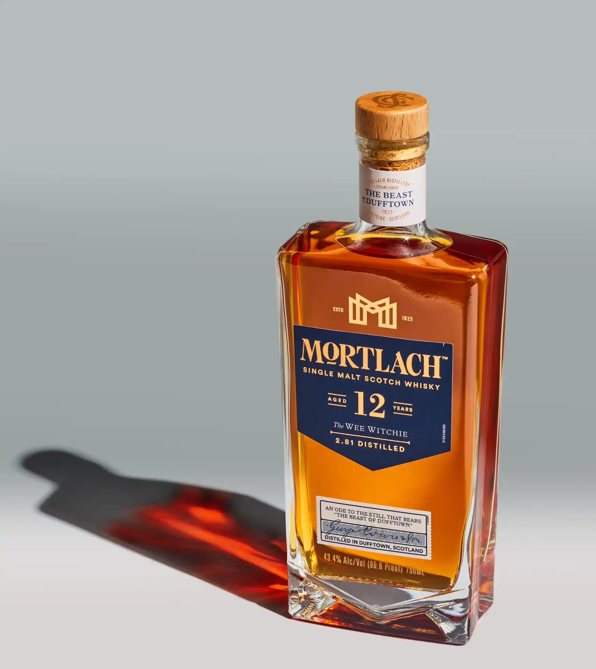 Een fles Mortlach single malt Scotch whisky staat op een sokkel voor een gouden en blauwe achtergrond.