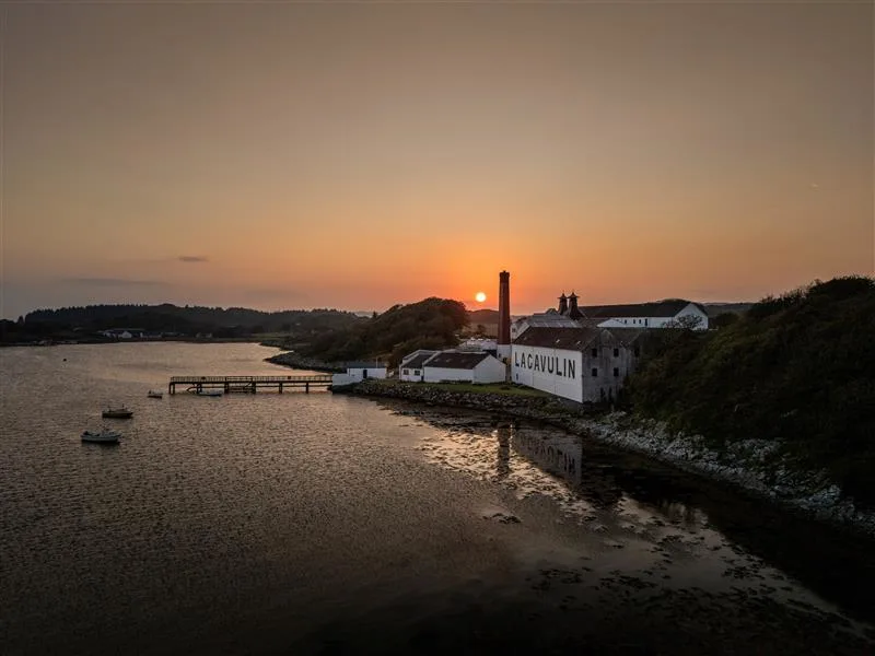 A drone taken photo of the Lagavulin Distillery with the sun setting behind it