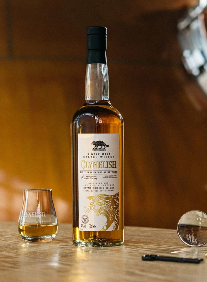 Een fles Clynelish naast een glas whisky op een glanzend koperen tafeltje.