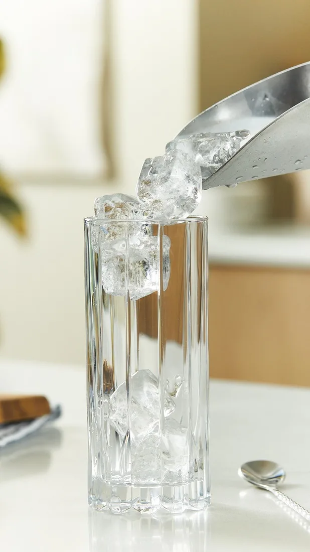 Ein silberner Barlöffel gießt Eis in ein Highball-Glas auf einem Küchentresen.  