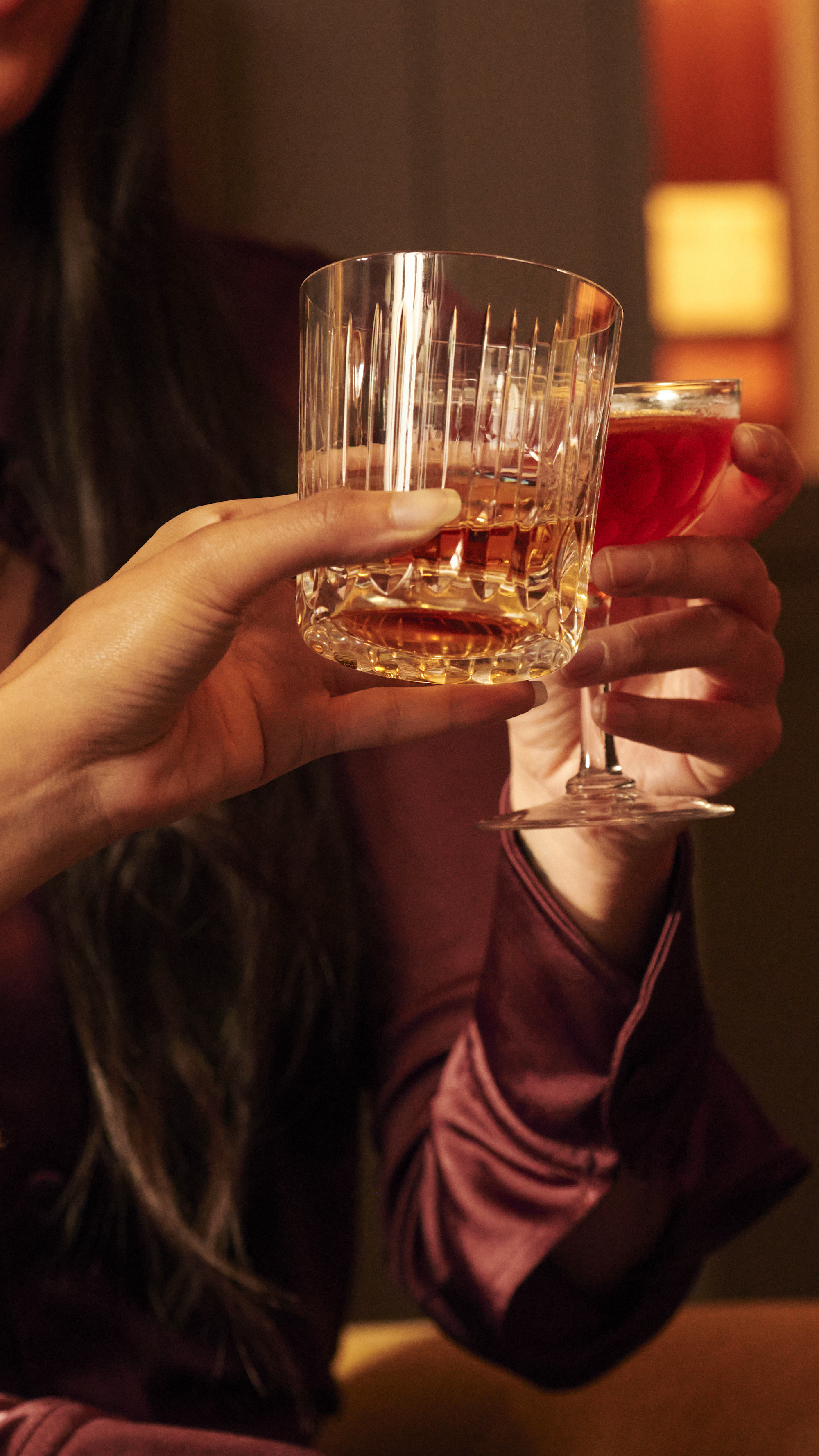 A close up image of people holding a glass of whisky in a tumbler with ice and a whisky cocktail