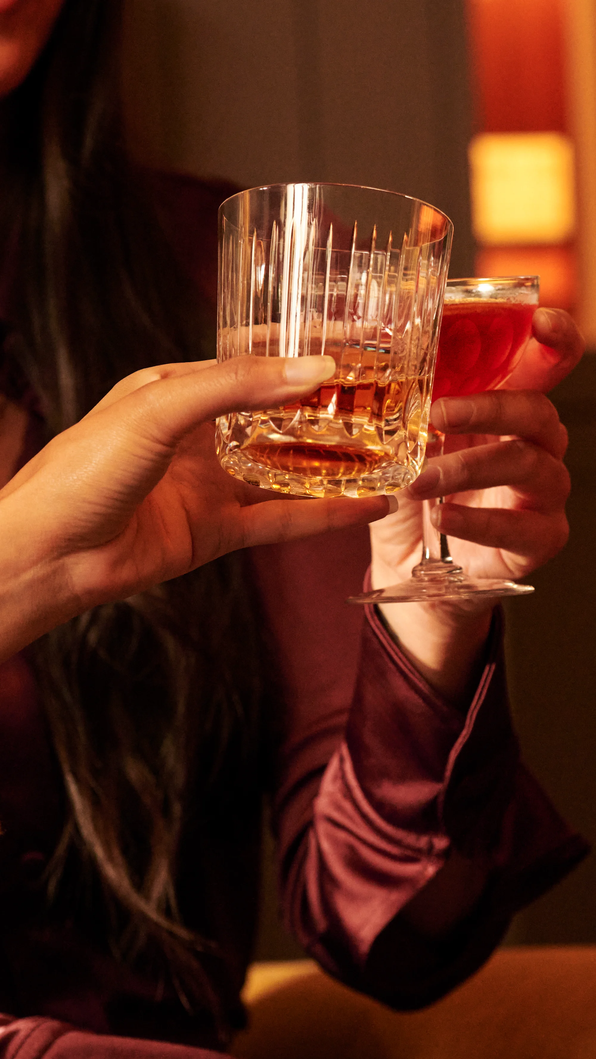 A close up image of people holding a glass of whisky in a tumbler with ice and a whisky cocktail
