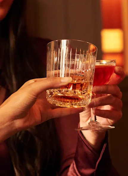 A close up image of people holding a glass of whisky in a tumbler with ice and a whisky cocktail