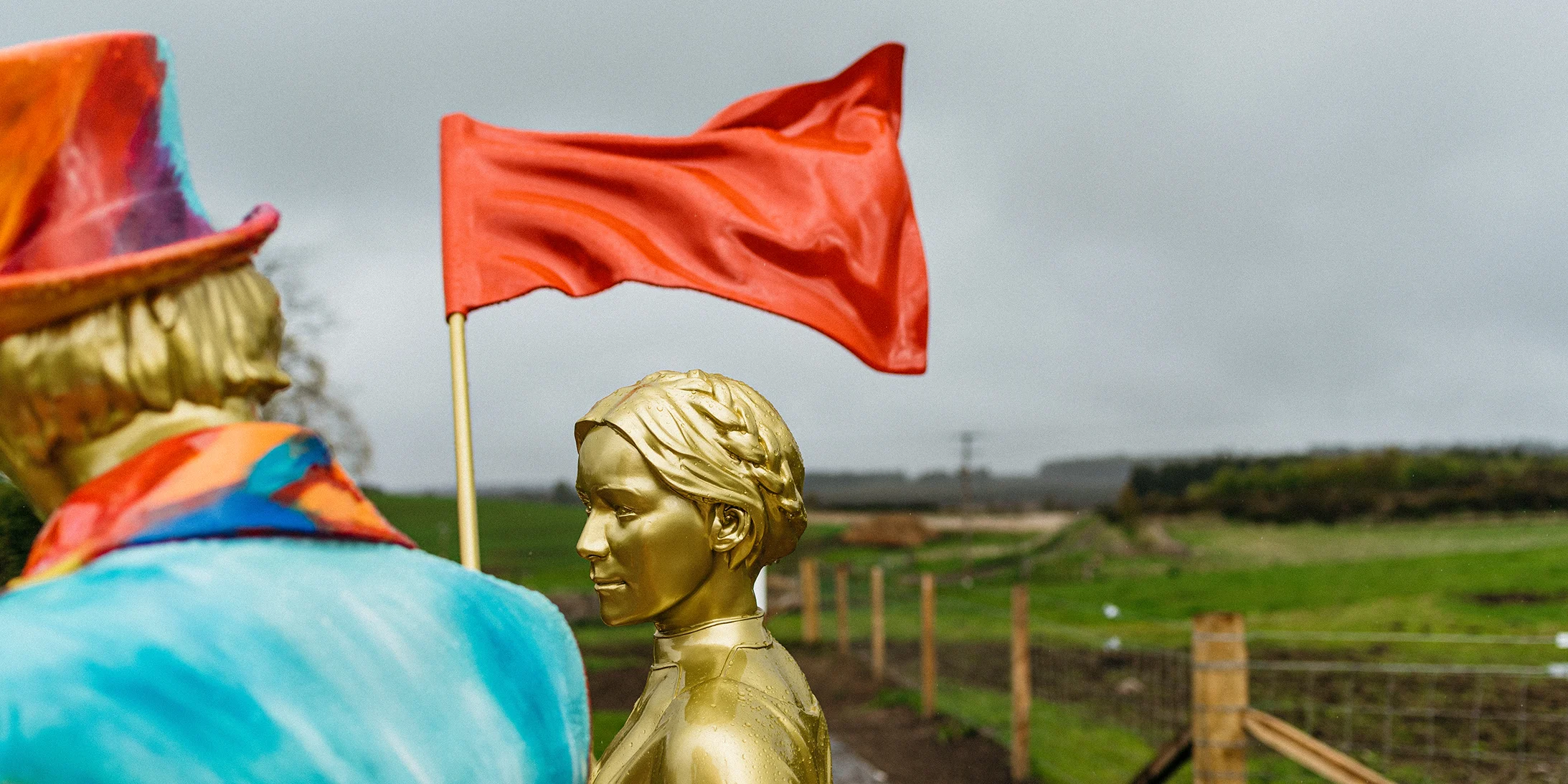 A golden statue of a Helen Cumming holding aloft a red flag, standing next to a statue of Johnnie Walker in a colourful jacket and top hat