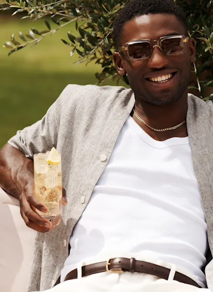 Ein Mann hält einen Whisky-Highball-Cocktail in der Hand, während er draußen in einem Garten sitzt