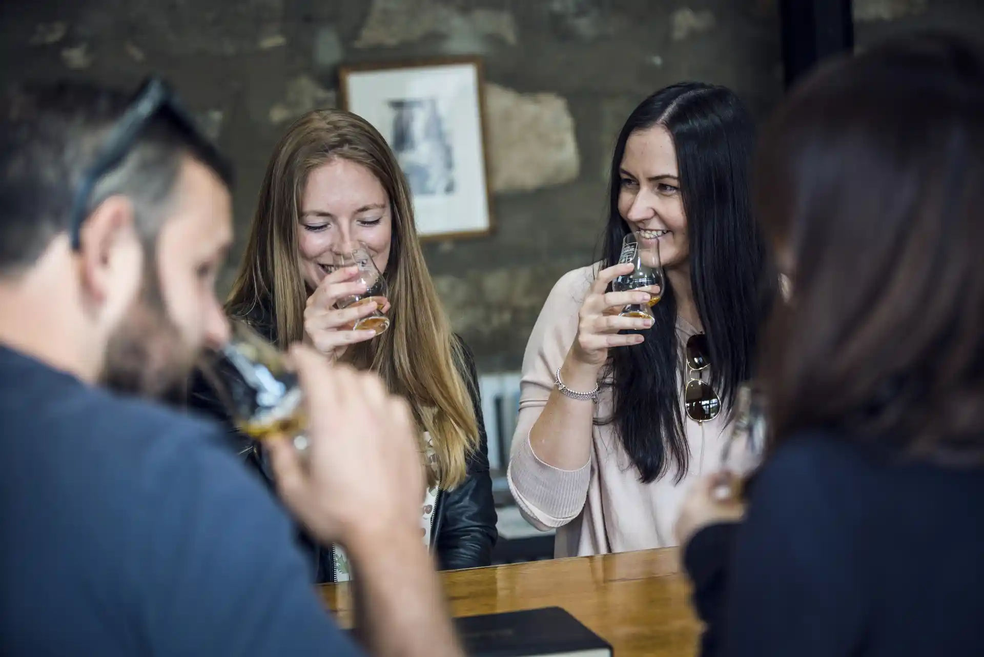 A group of people hold dram glasses containing whisky up to their noses.