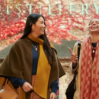 Two female friends stand in front of Blair Athol distillery, laughing together