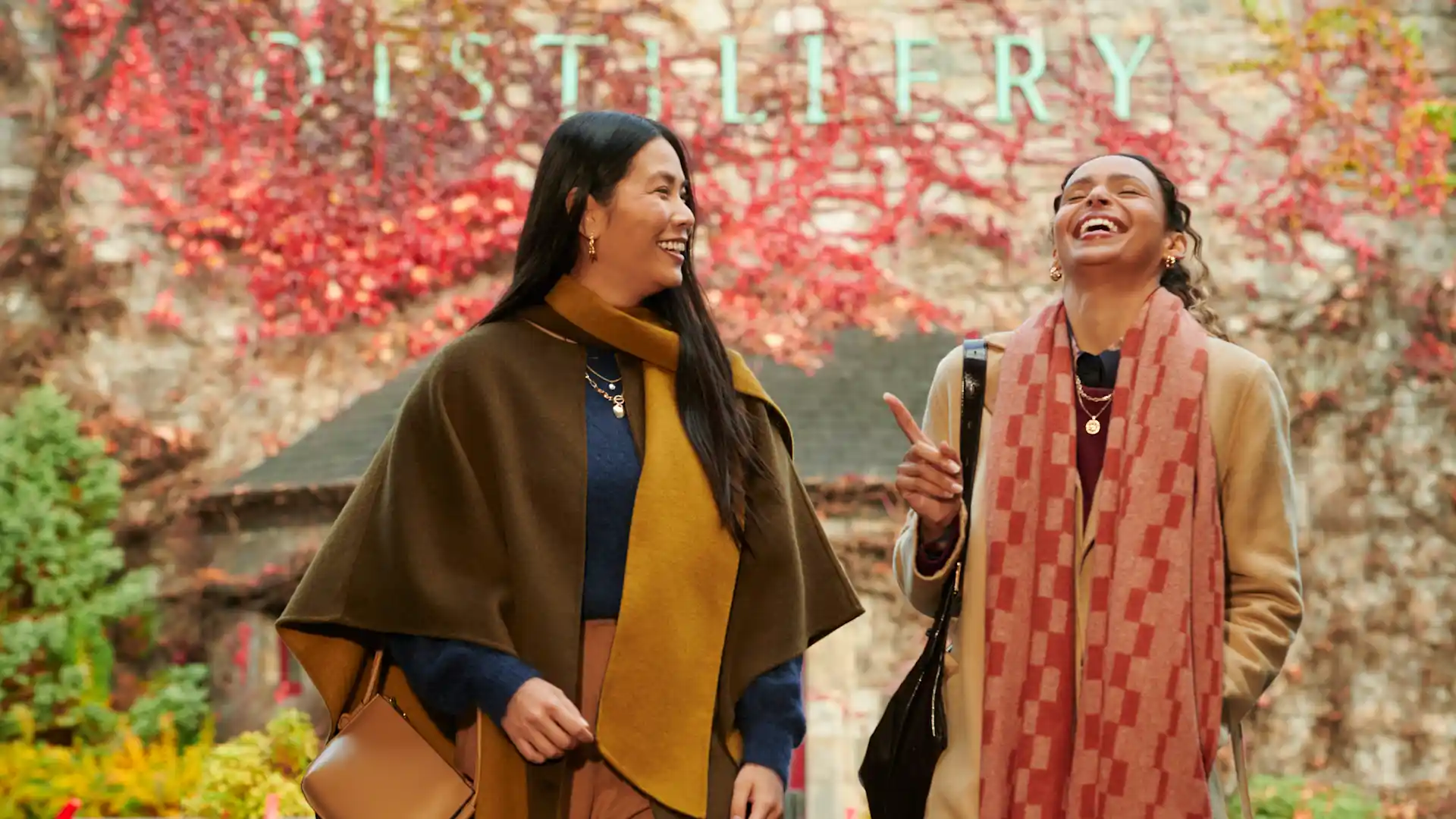 Two female friends stand outside Blair Athol distillery, laughing and joking together