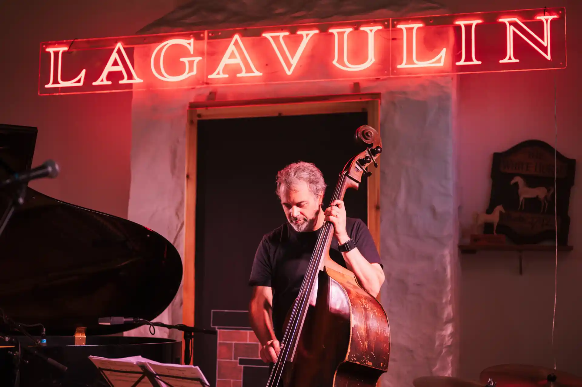 Musician playing double bass in front of a neon sign written Lagavulin