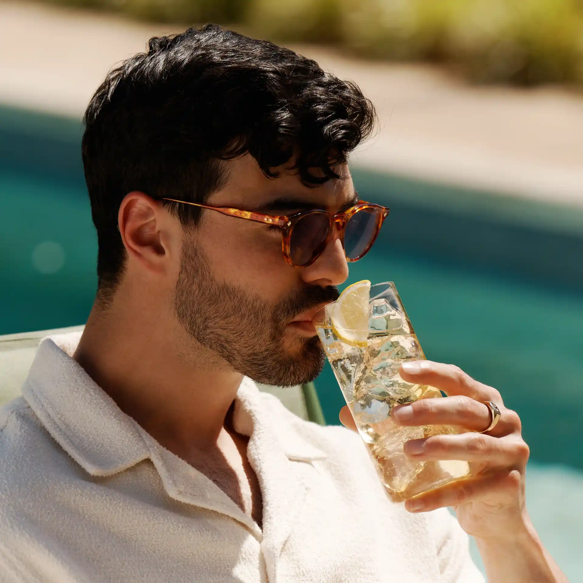 A man sits by a pool sipping a whisky highball cocktail