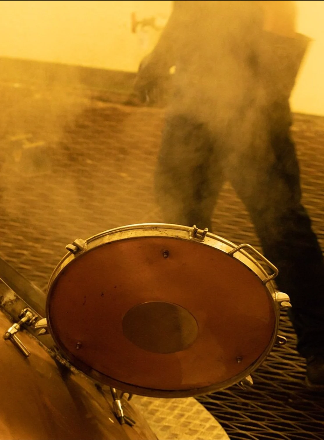 Ein Mann geht an einer kupfernen Brennereimaschine mit offener Luke vorbei.