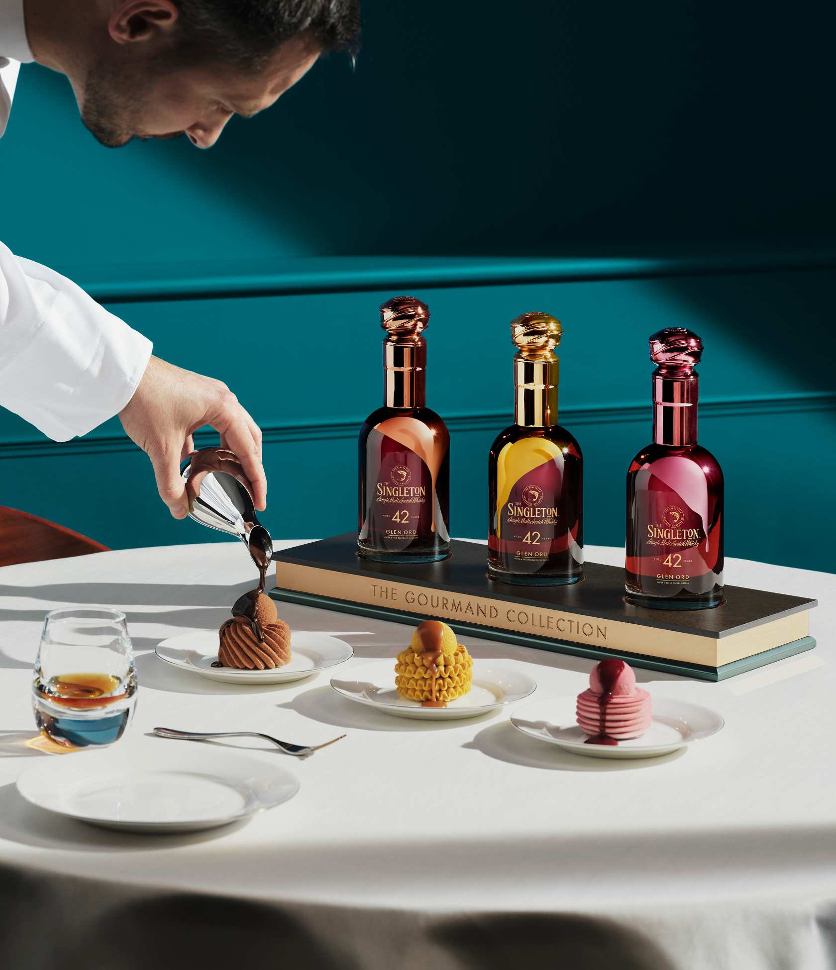 Chefkoch Nicolas Rouzaud übergießt ein Dessert mit einer Sauce und stellt die Flaschen The Singleton Gourmand Collection neben drei Desserts und einem Glas Whiskey aus.