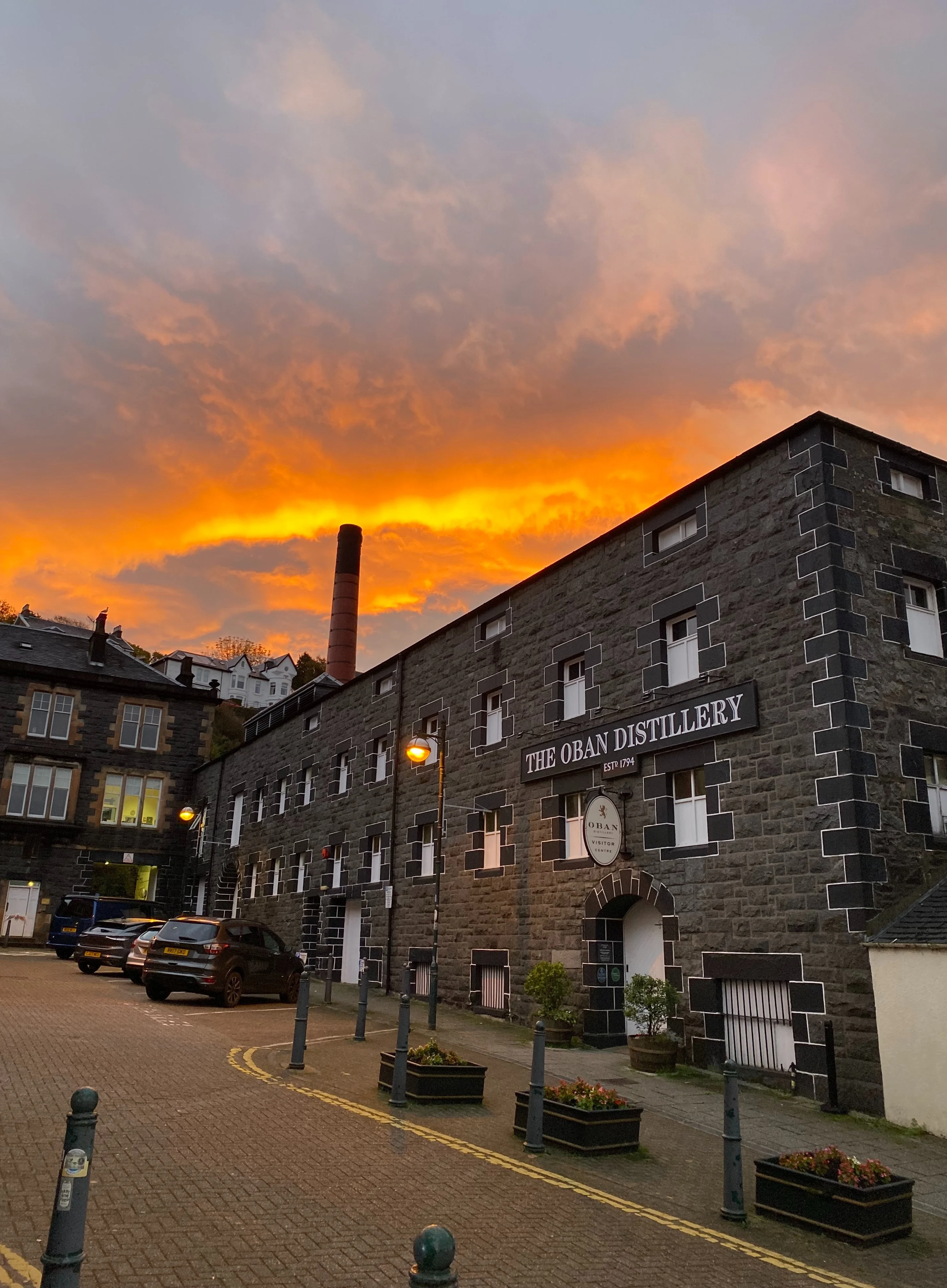 Orange sunset behind brick building with the sign 'Oban Distillery'.