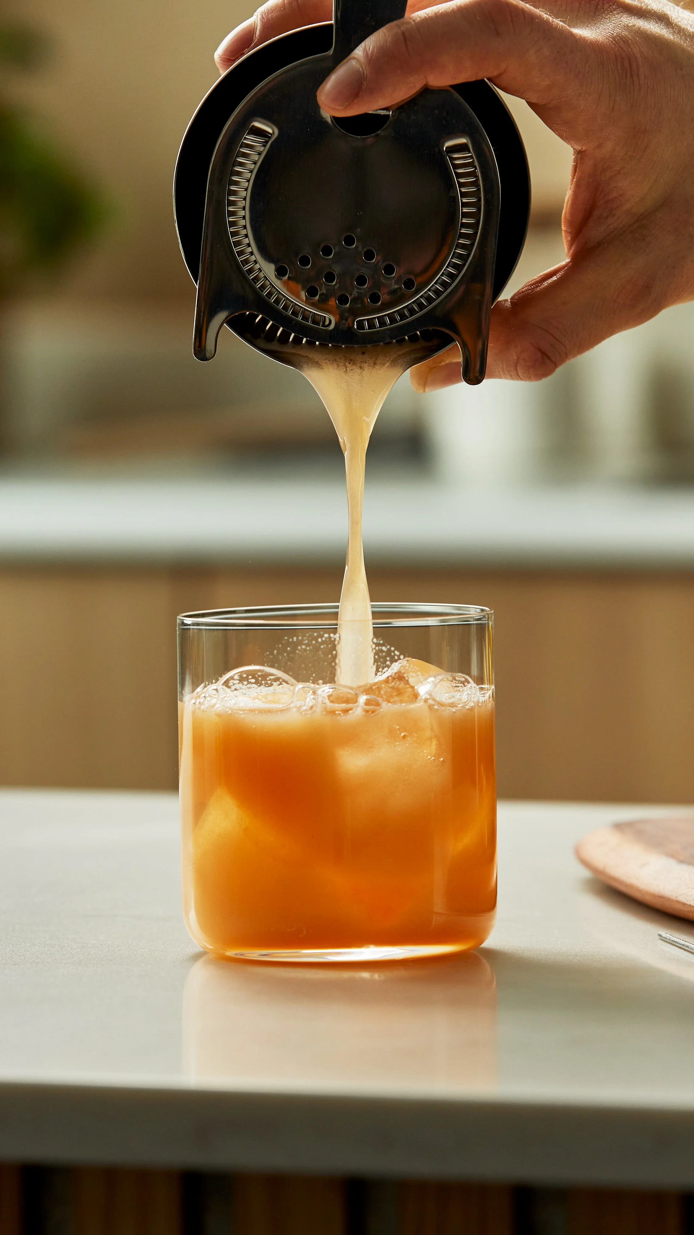 Iemand die een whisky sour in een glas met ijs schenkt