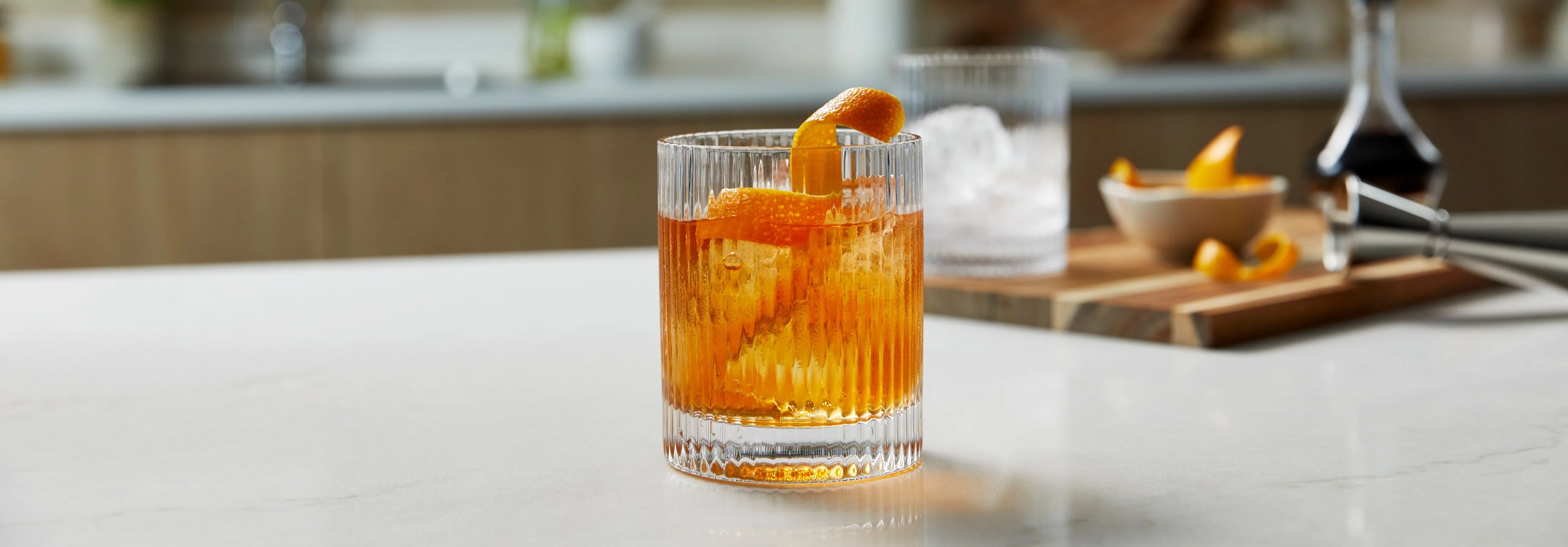 An Old Fashioned cocktail in a rocks glass, filled with ice and topped with an orange garnish.