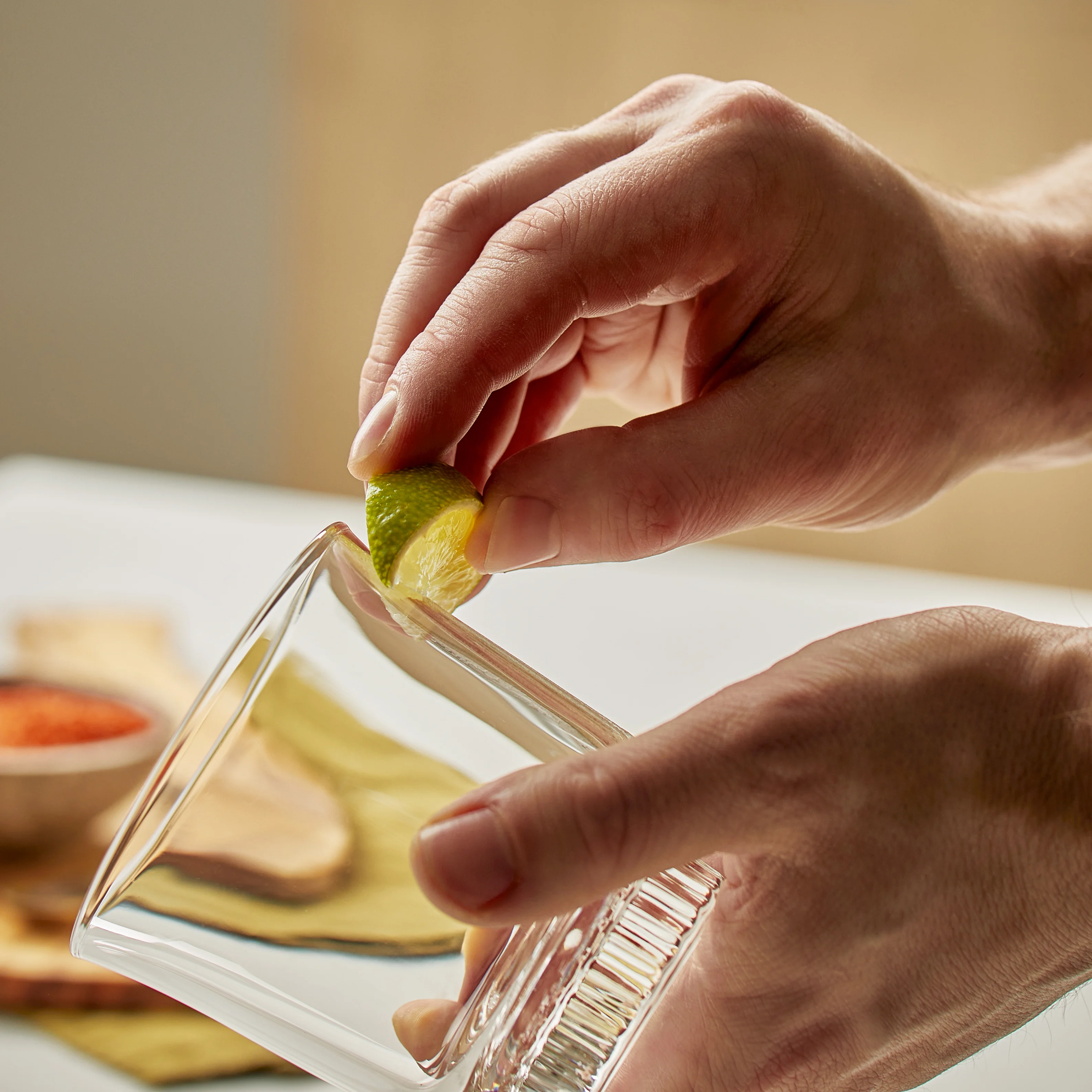Hands rub a cut lime on a rocks glass in preparation for a margarita. 